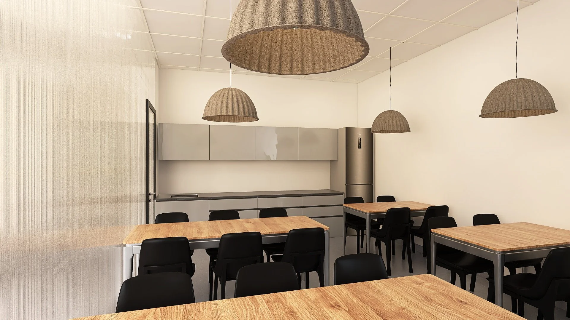 Sala de descanso o comedor con mesas de madera, sillas negras, iluminación con lámparas de techo de fibra, cocina moderna en el fondo y pared blanca.