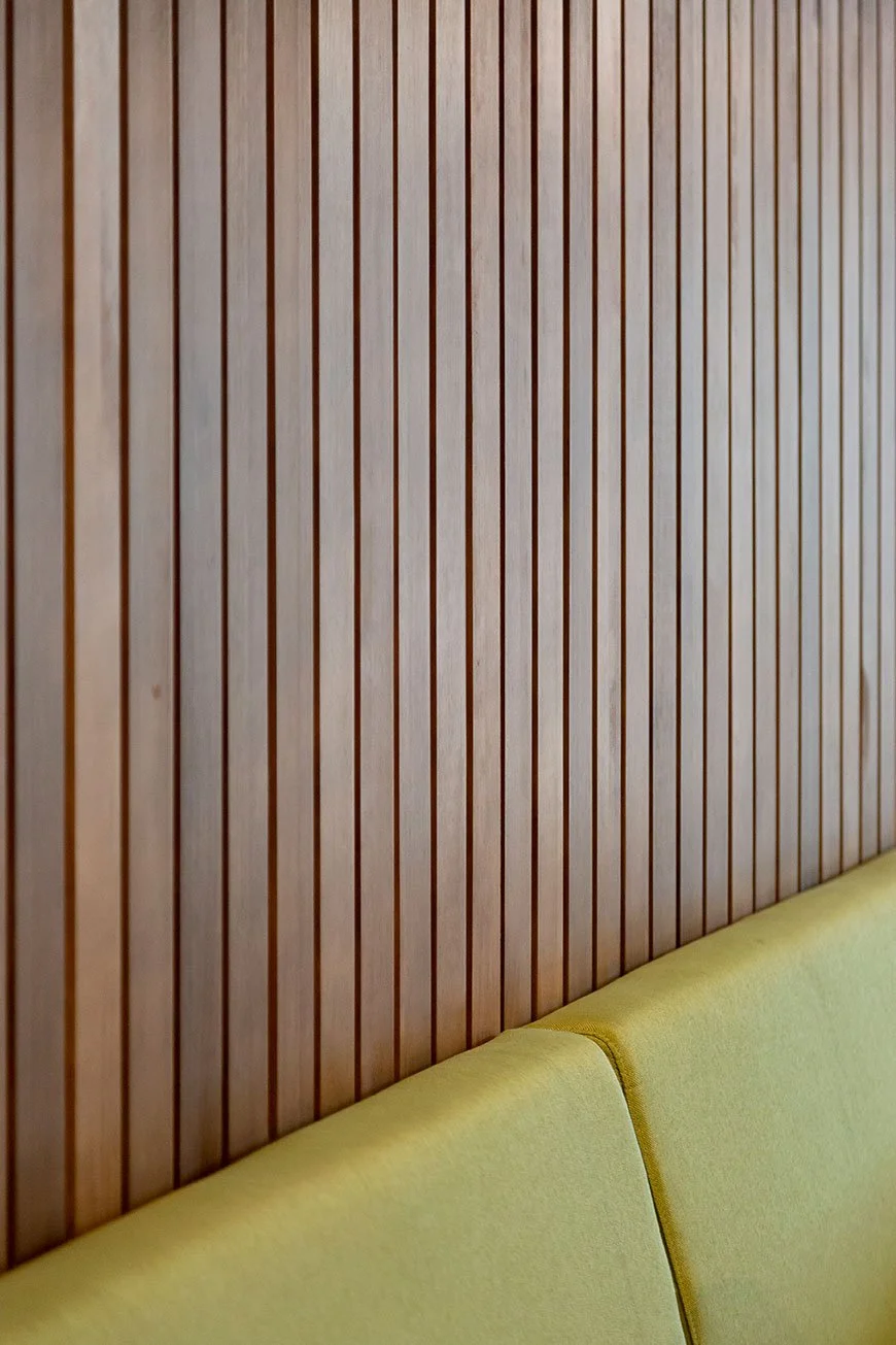 Panel de madera con listones verticales y sofá amarillo en la parte inferior. Diseño de interiorismo comercial. Retail design. Diseño de bares y restaurantes. Foto de Eva Carasol.