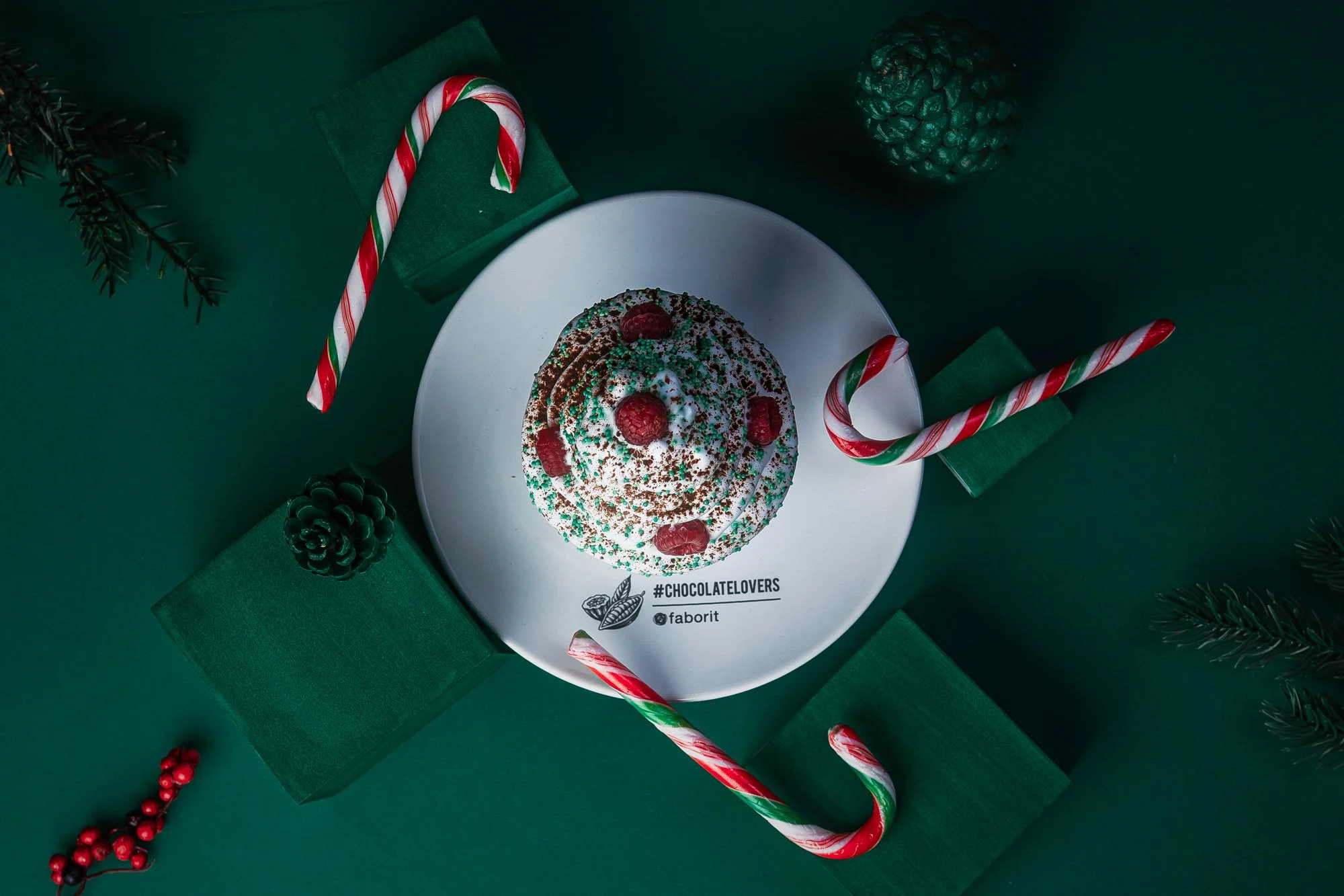 Postre de chocolate navideño con crema, frambuesas y bastones de caramelo en fondo verde.