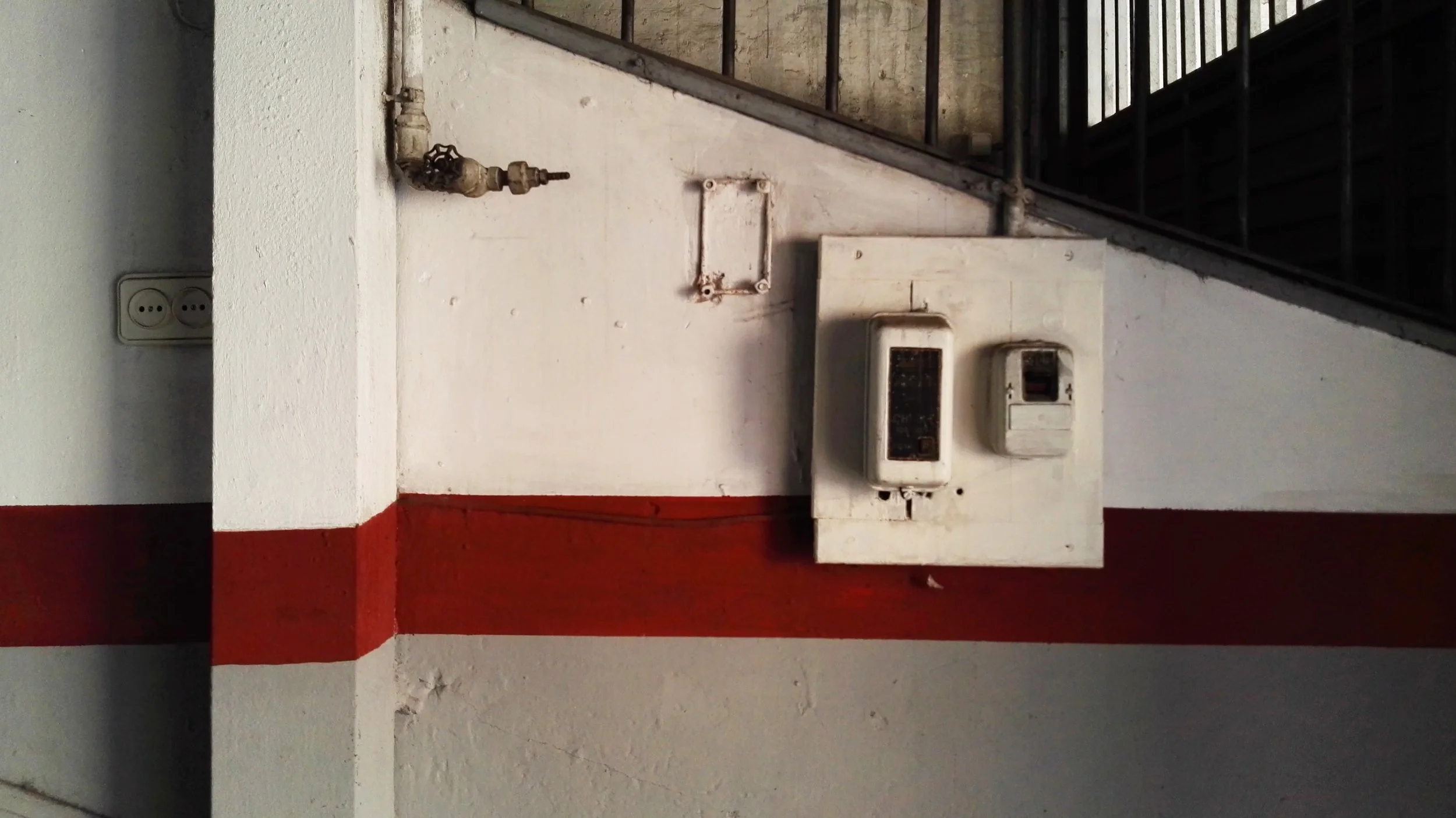 Decoración con pared blanca y roja, enchufe, llave de agua, medidor de electricidad y cables