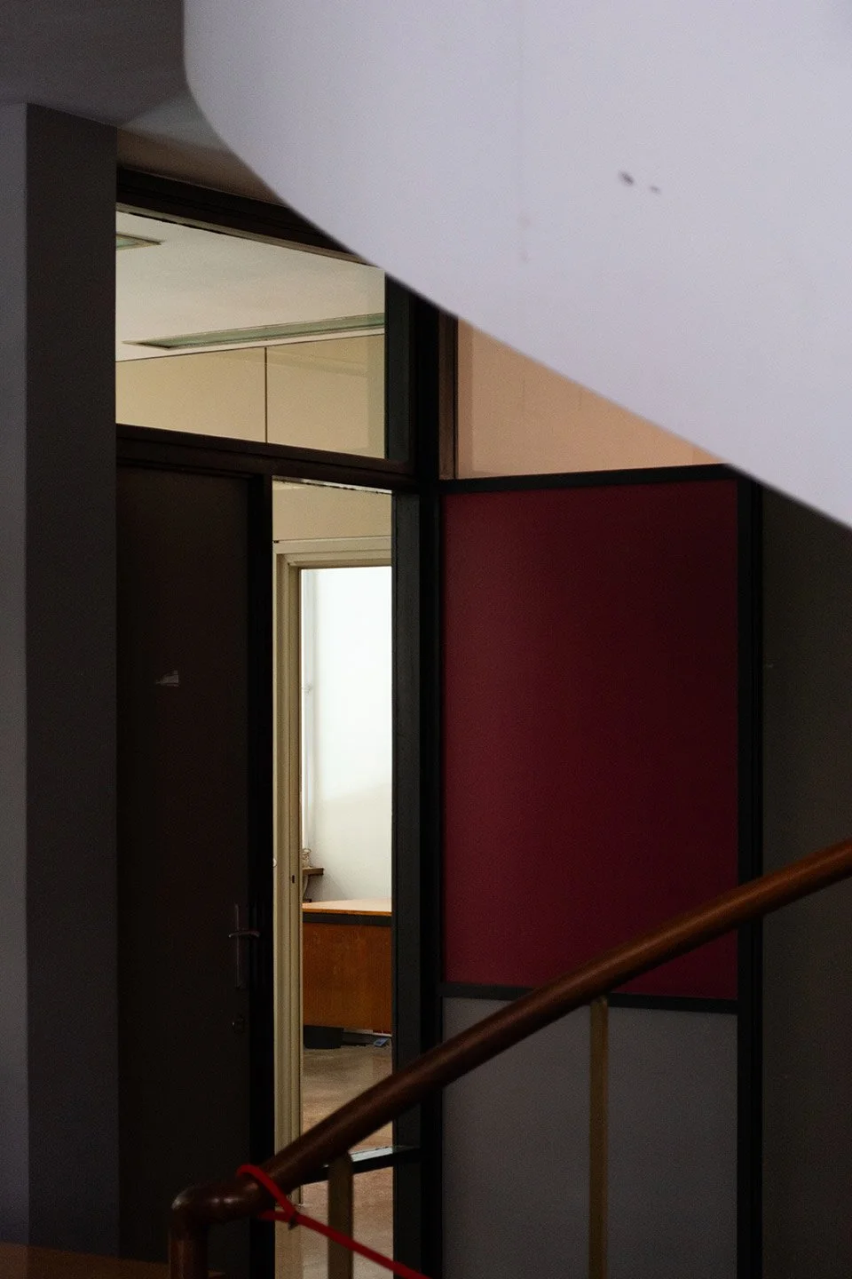 Vista de un interior de casa mostrando una escalera de madera y paredes decoradas con paneles de colores y ventanas.