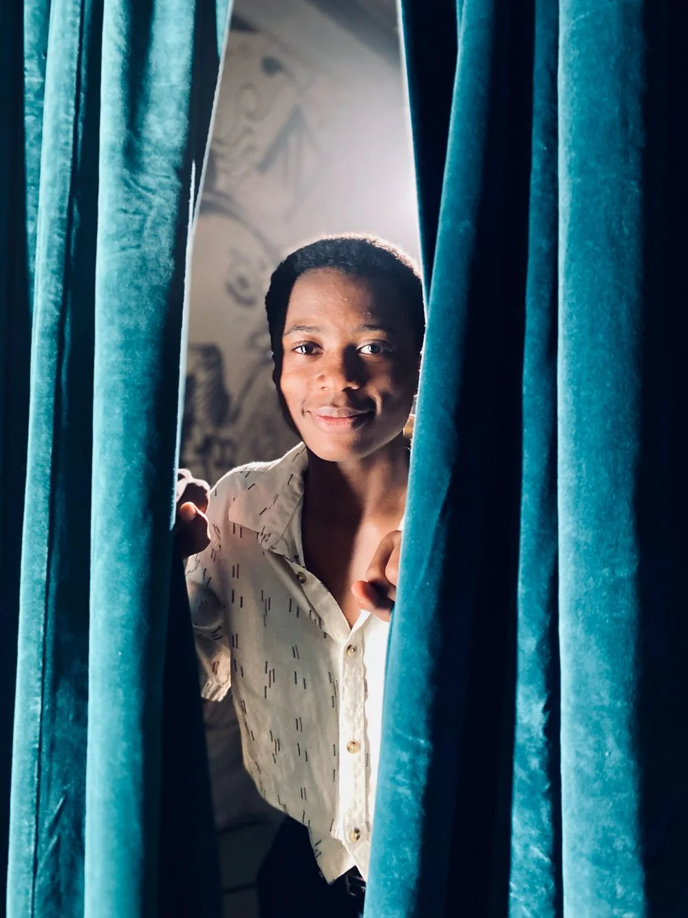 Still from documentary re-creation: a young woman peeking through blue curtains with a warm smile.