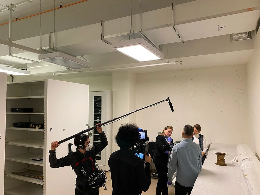 Filming crew recording interview with two women and a man in an office setting.