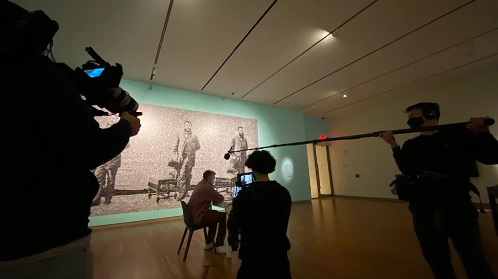 People filming a black-and-white large photograph or artwork in an art gallery or museum.
