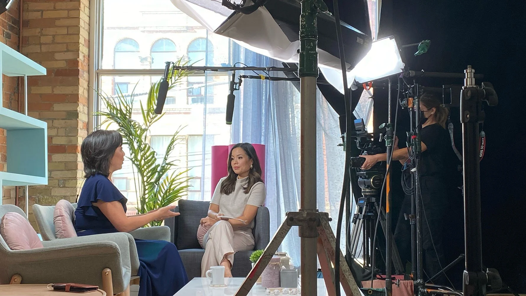 A woman interviewing another woman in a studio setting with camera and lighting equipment.