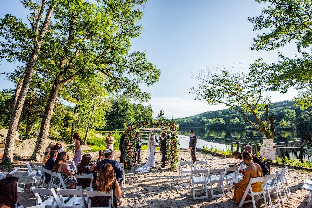 Groom and bride say vows under trellis on beach with lake view