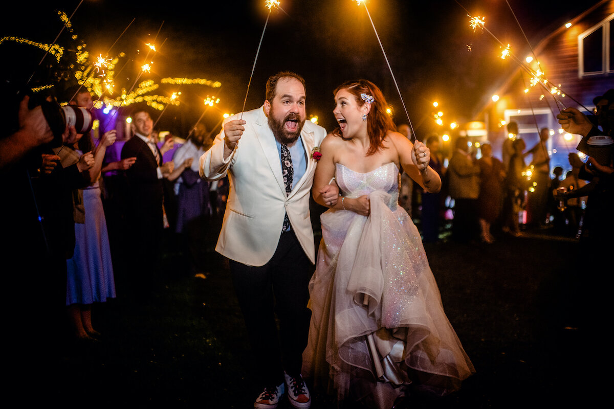 Bride and groom exit venue while guests hold sparklers 