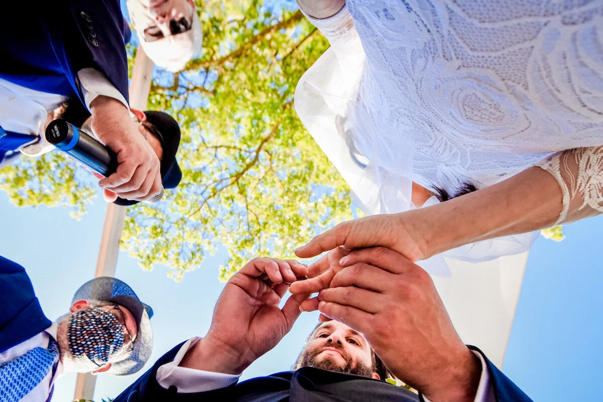 View from below of groom placing wedding ring on bride's ring finger