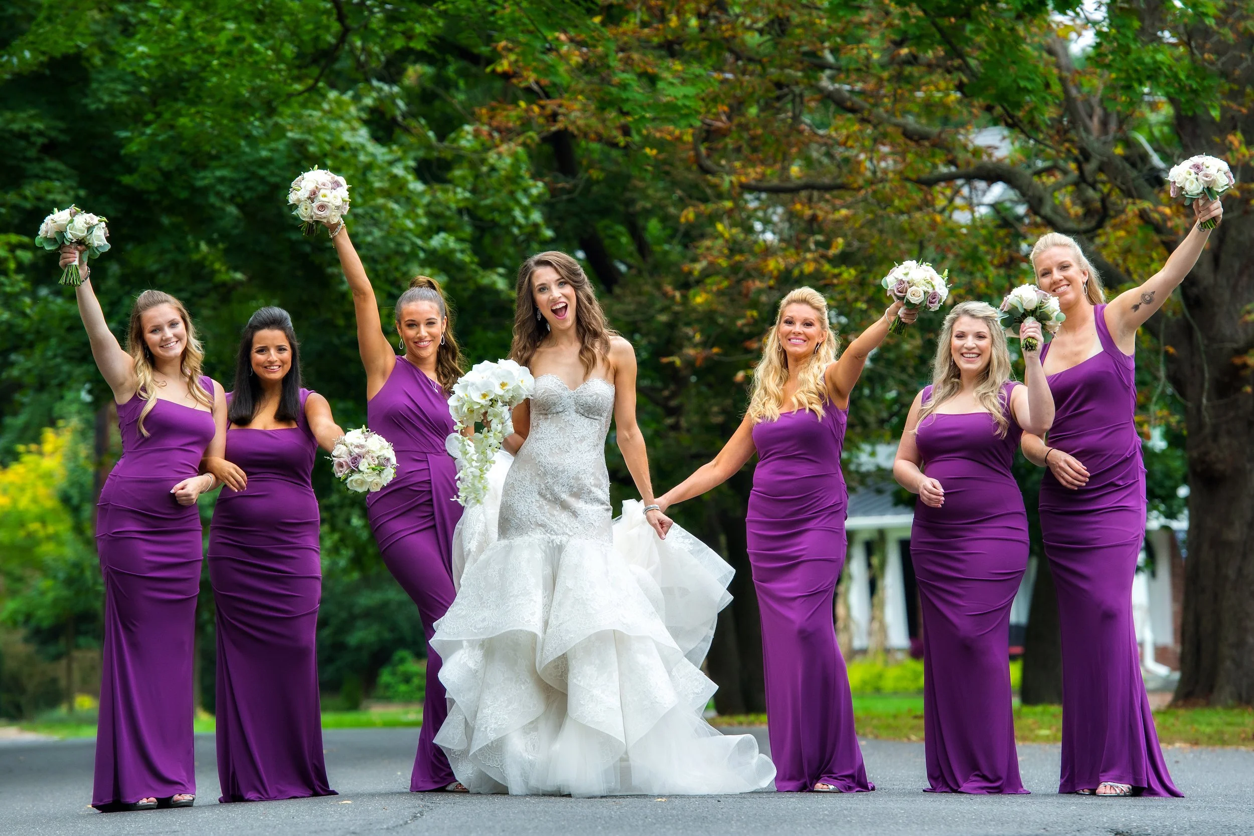 Bride and bridesmaids in purple dresses pose outside venue