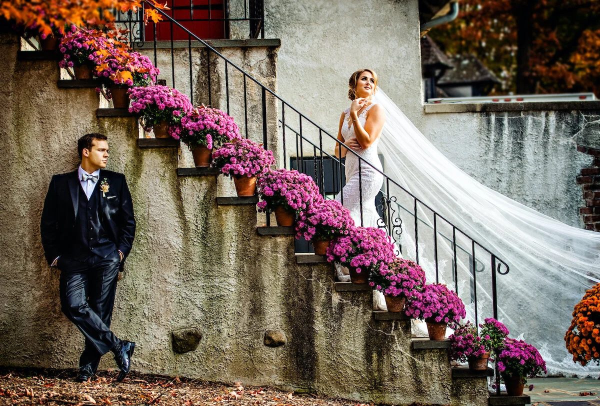 Bride poses on Chateau stairs with flowing veil as groom poses beside stairs