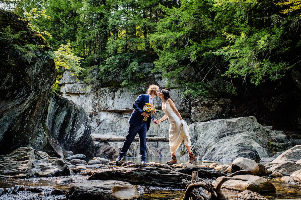 Bride and groom lean in for kiss at foot of creek
