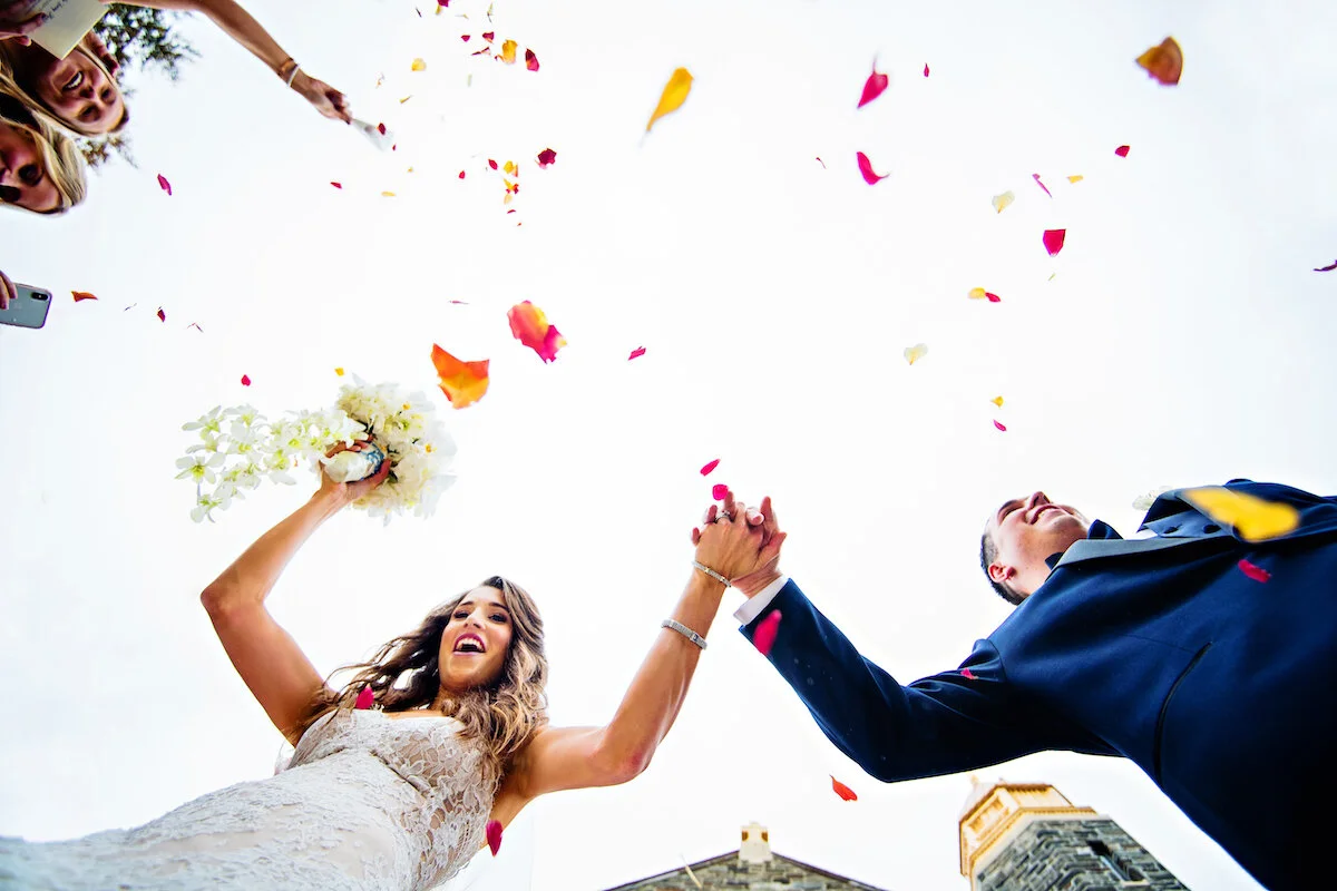 View from below of bride and groom holding hands as flowers are thrown
