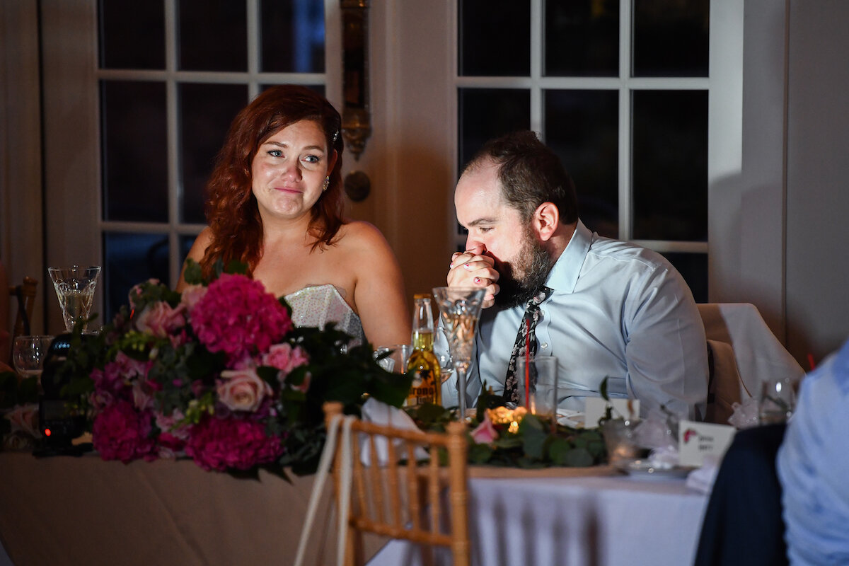 Groom kisses bride's hand as they emotionally listen to speeches