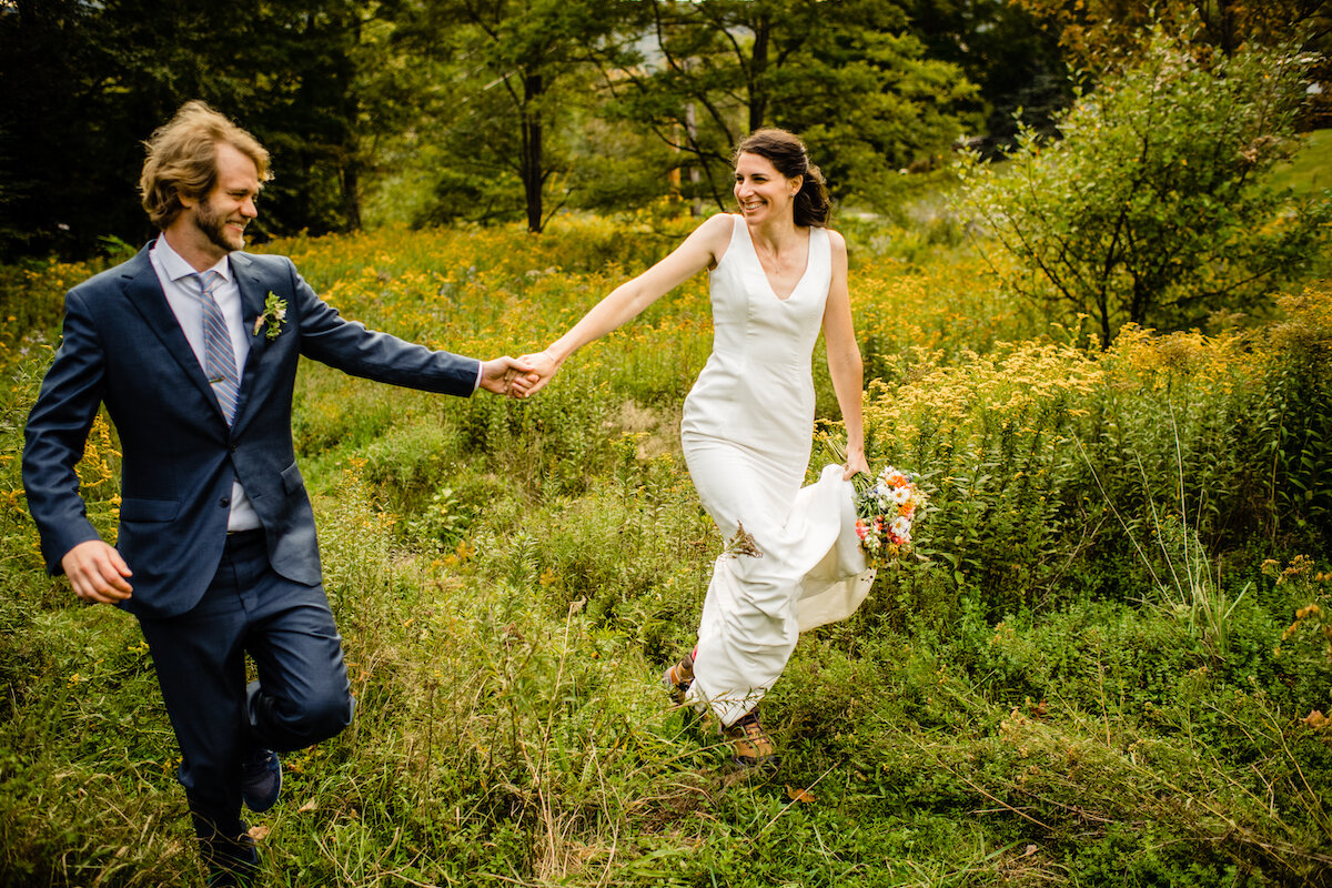 Bride and groom walk and hold hands in meadow field
