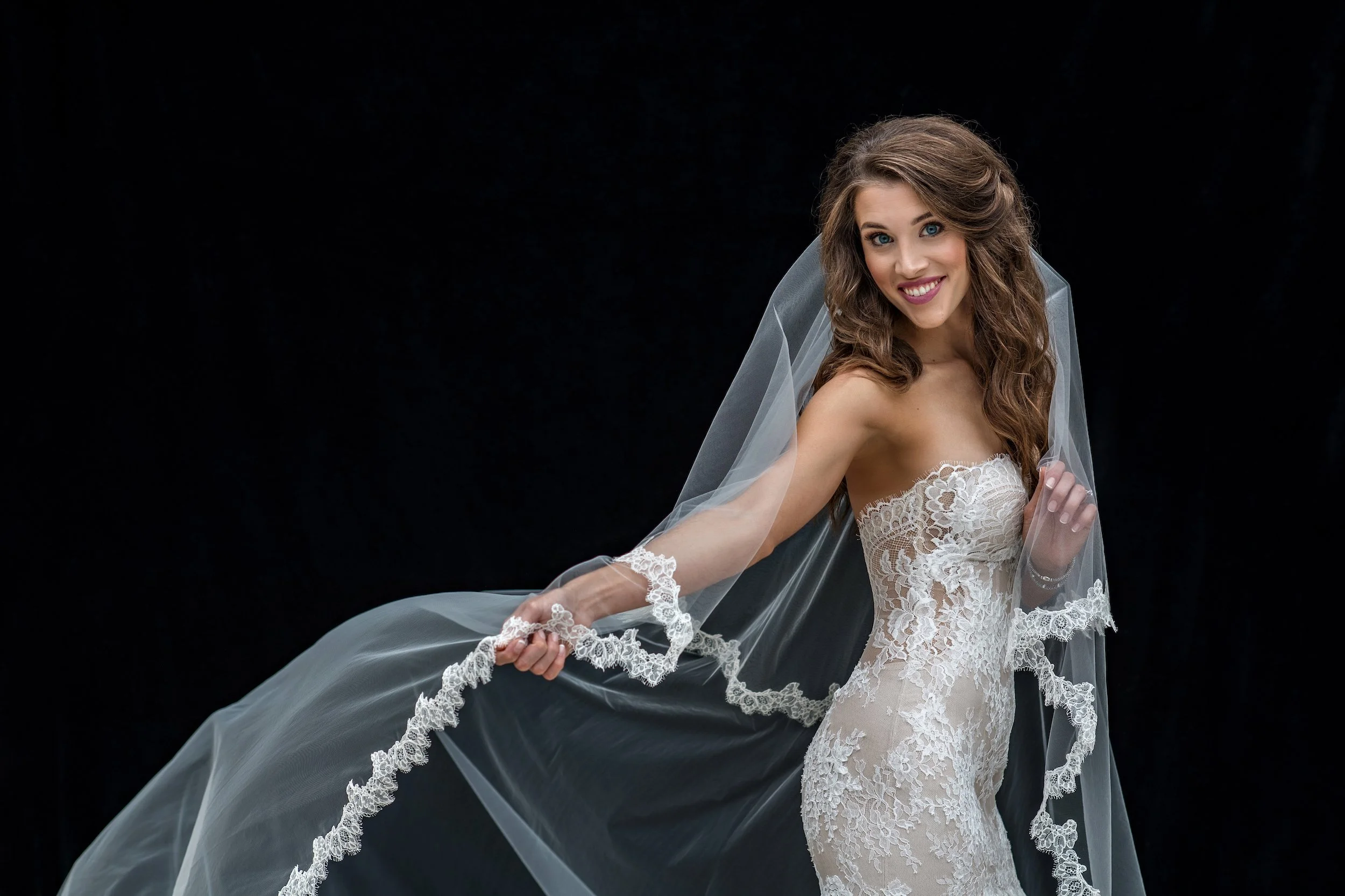 Bride posing in wedding dress and veil with black background