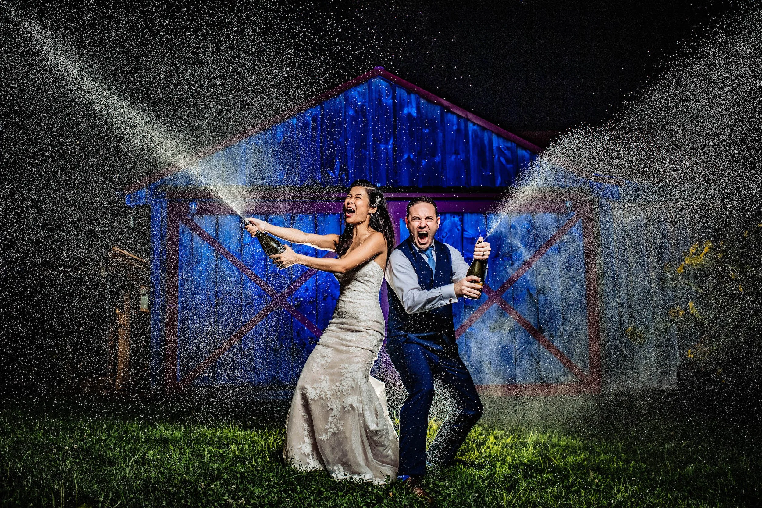 Bride and groom open shaken champagne bottles at end of night