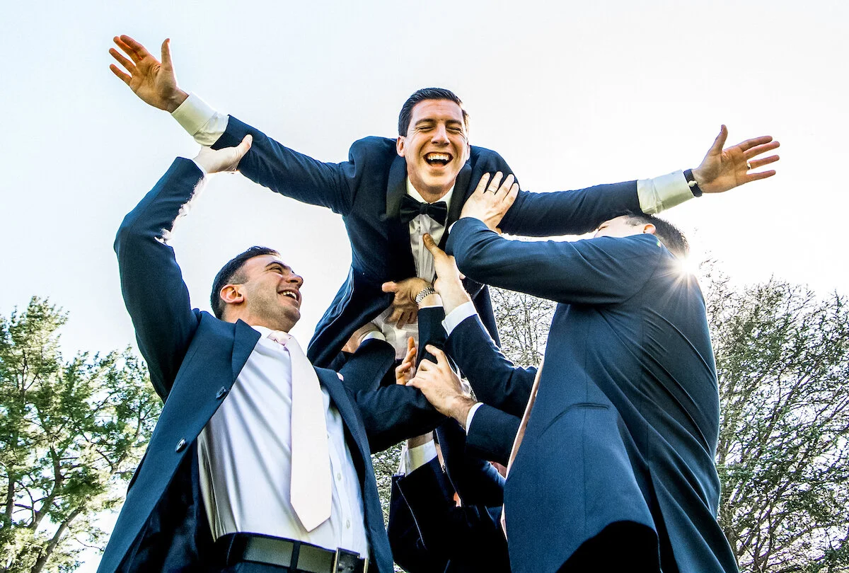 Laughing groom being held up by groomsmen