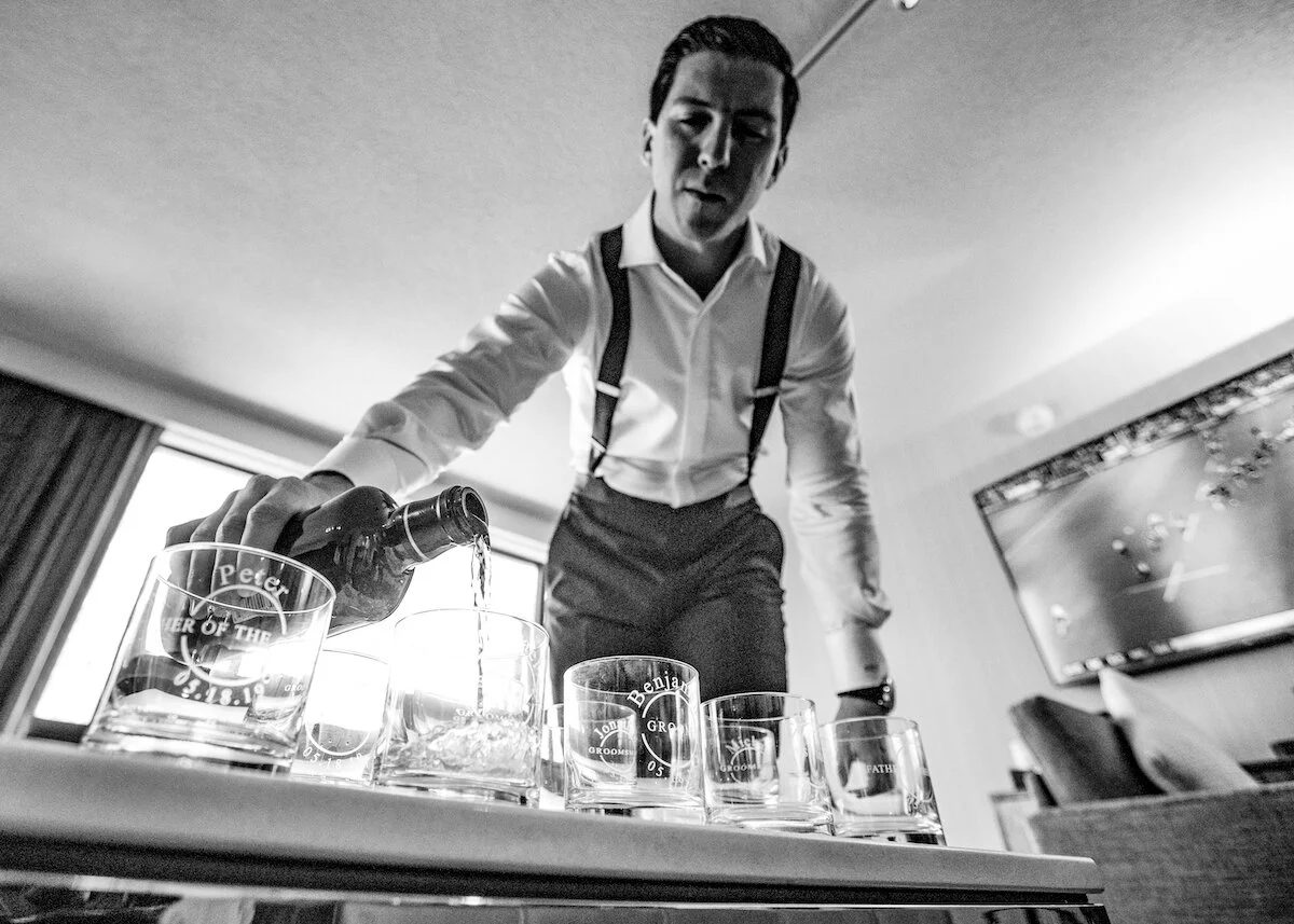 Groom filling engraved glasses with whiskey