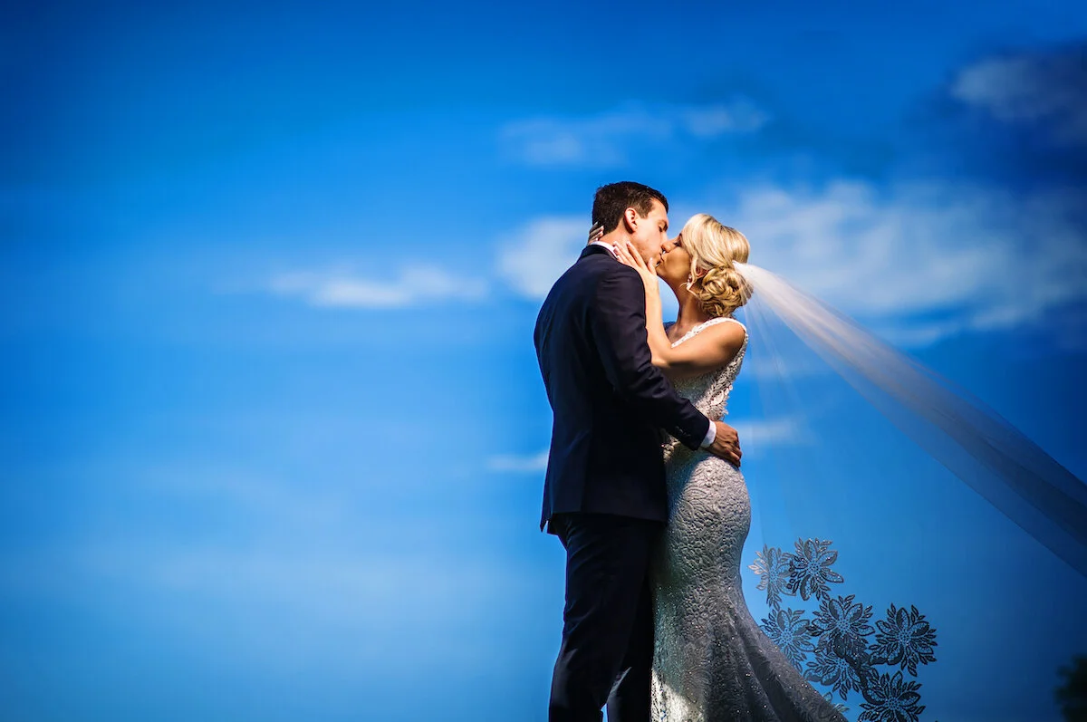 Bride and groom kiss in front of blue skies