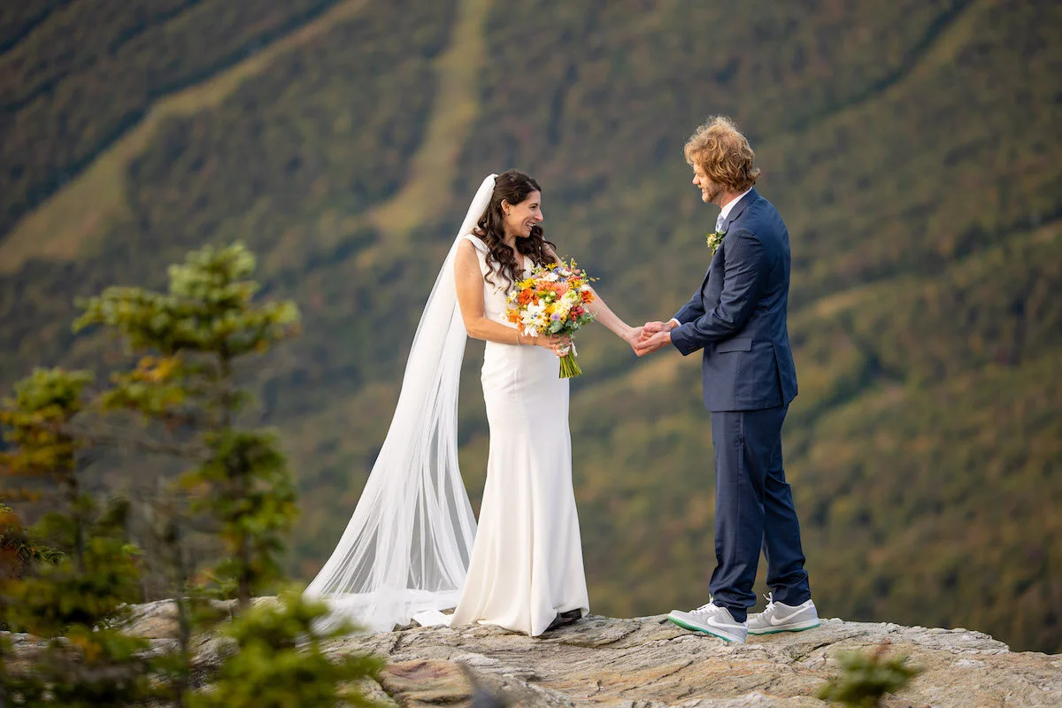 Groom places ring on bride's hand at top of mountain