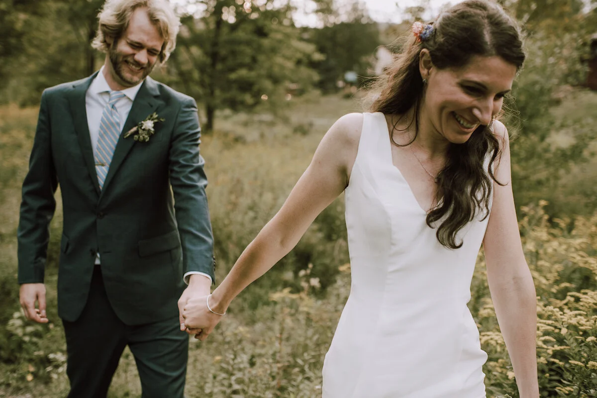 Bride leads groom in meadow