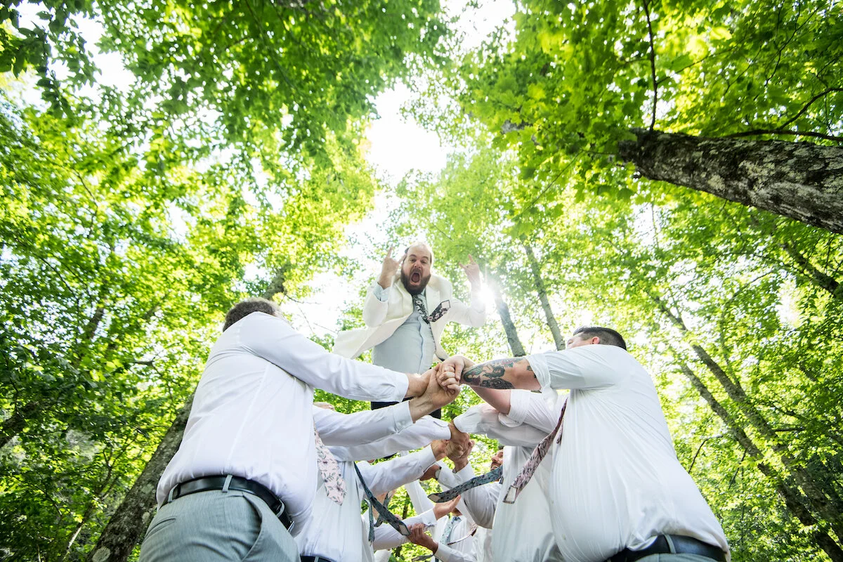 Groom mid-jump into groomsmen arms