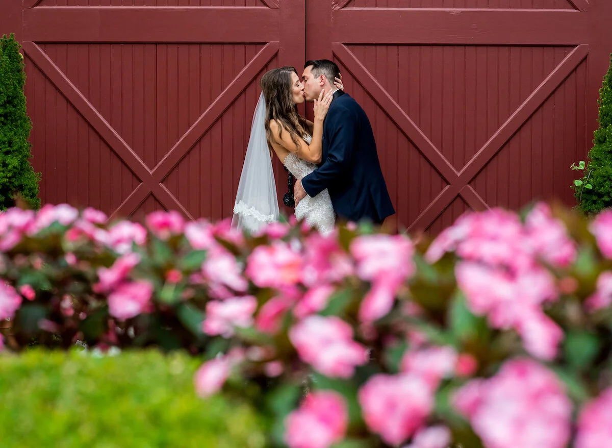 Bride and groom intimately kiss old fashioned red barn door in background