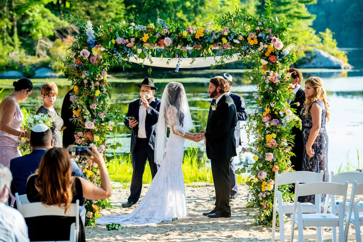 Bride and groom hold hands under trellis lake view in background