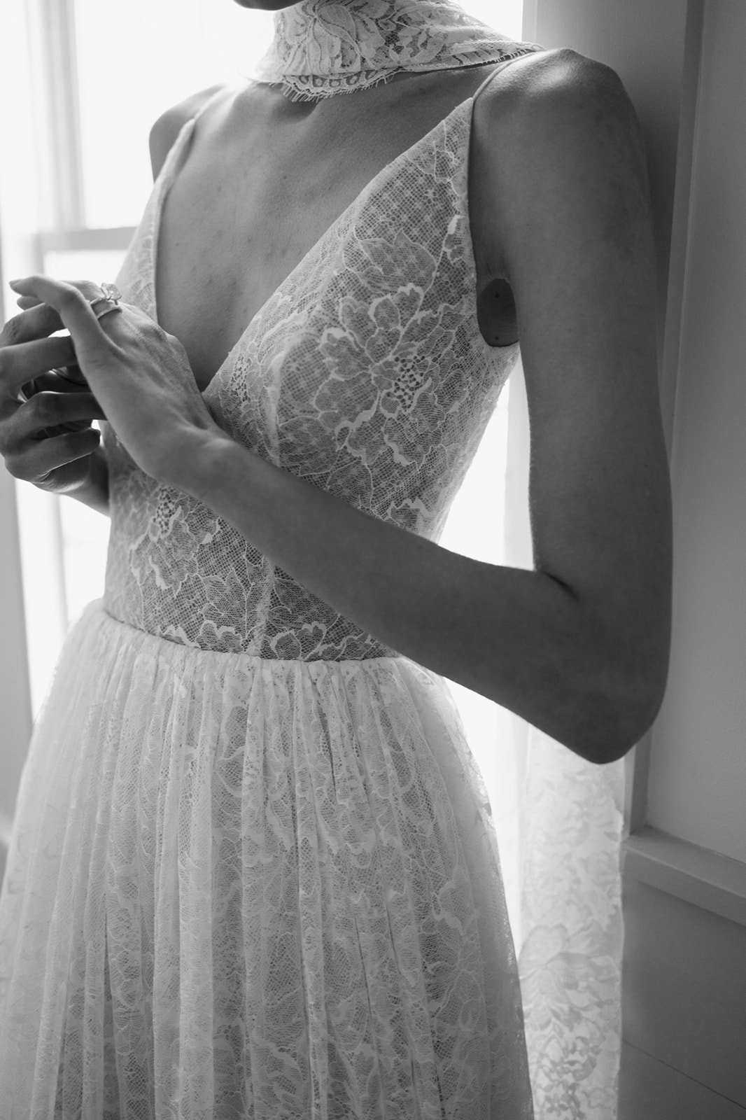 Woman in a white dress holding a bouquet of white flowers, standing indoors near a window.