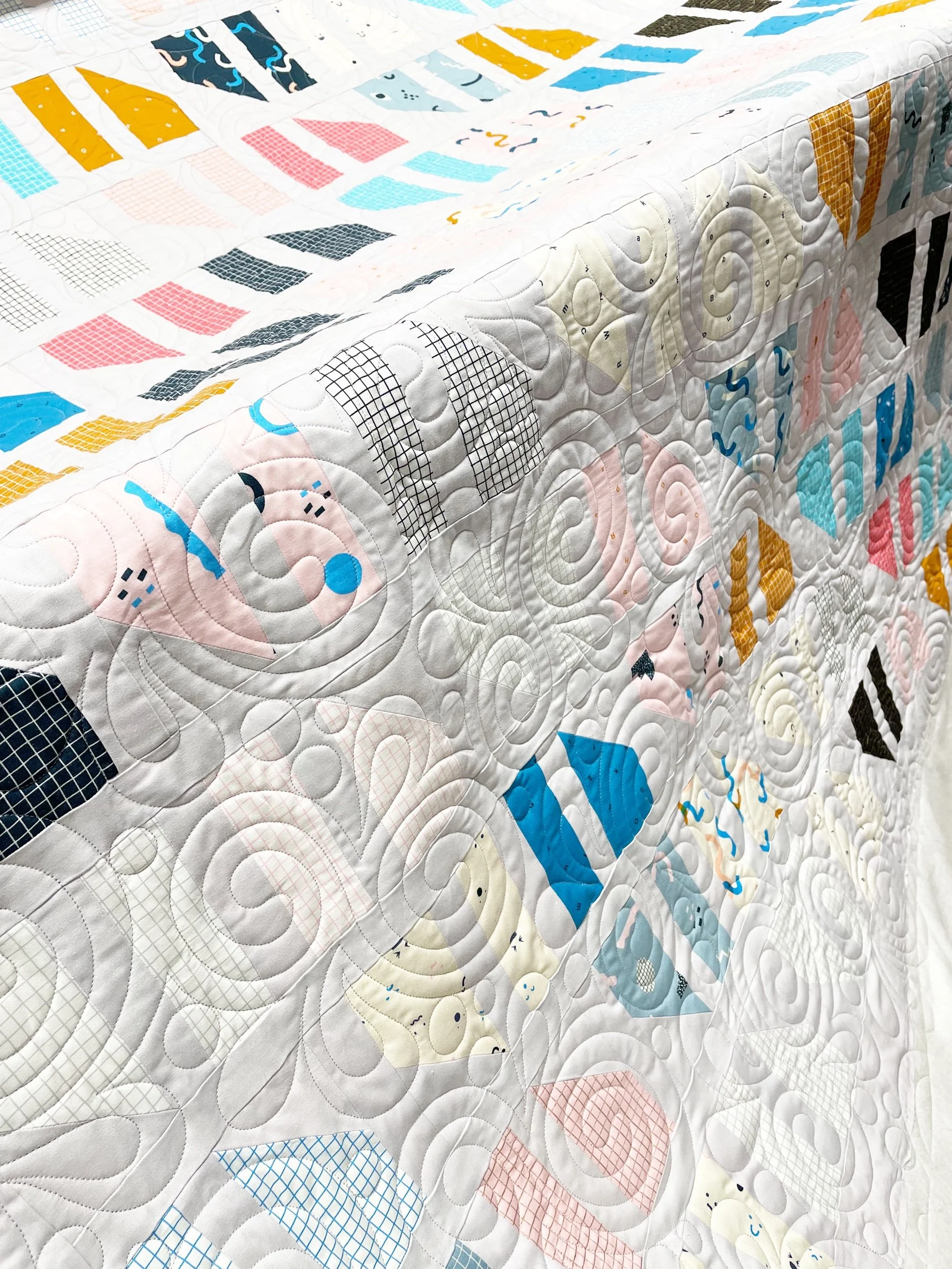Close-up of a colorful quilt with geometric patterns and swirl stitching, draped over a surface.