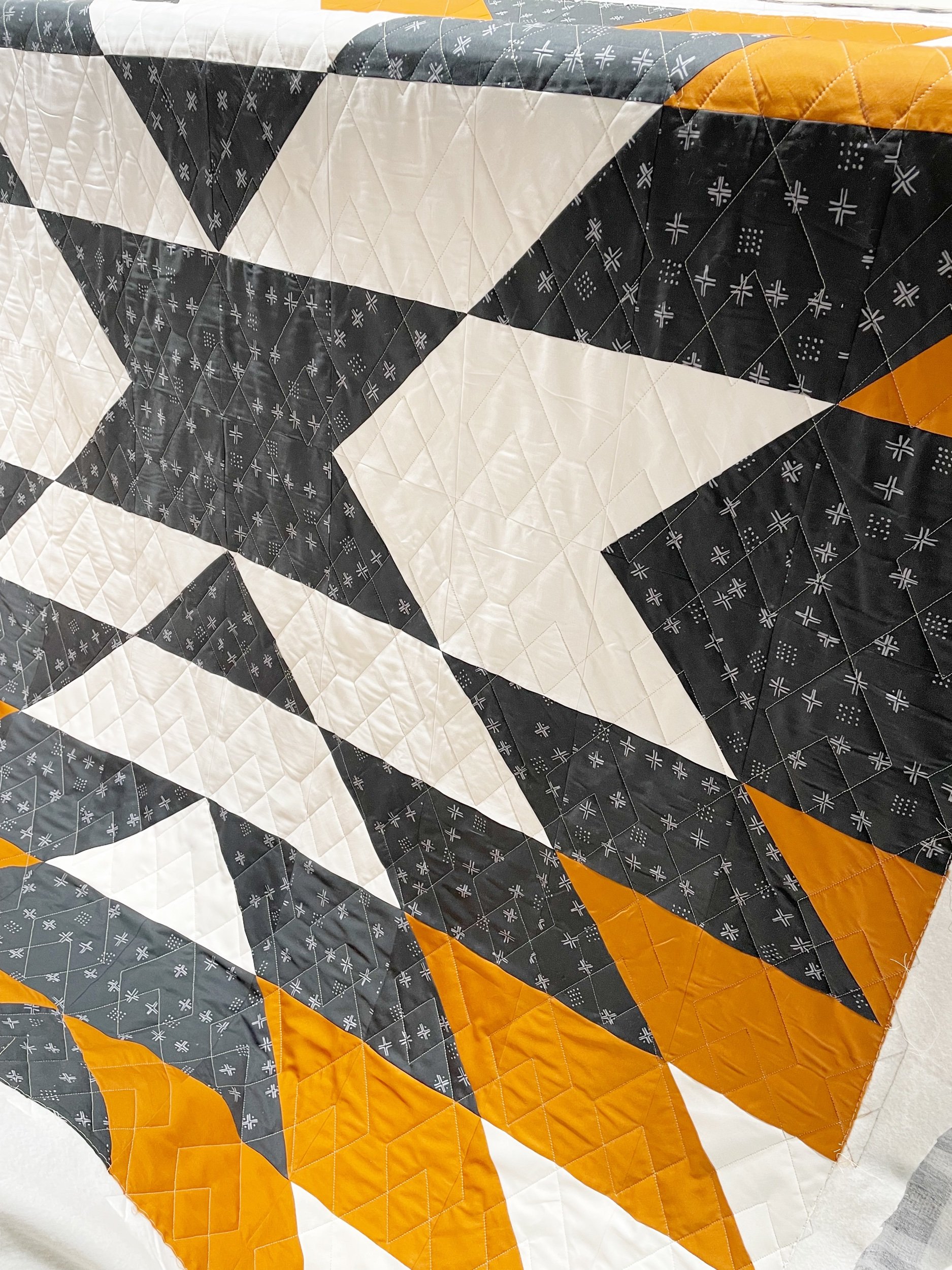 Close-up of a geometric quilt with black, white, gray, and orange fabric sections featuring various patterns, including small crosses and dots.