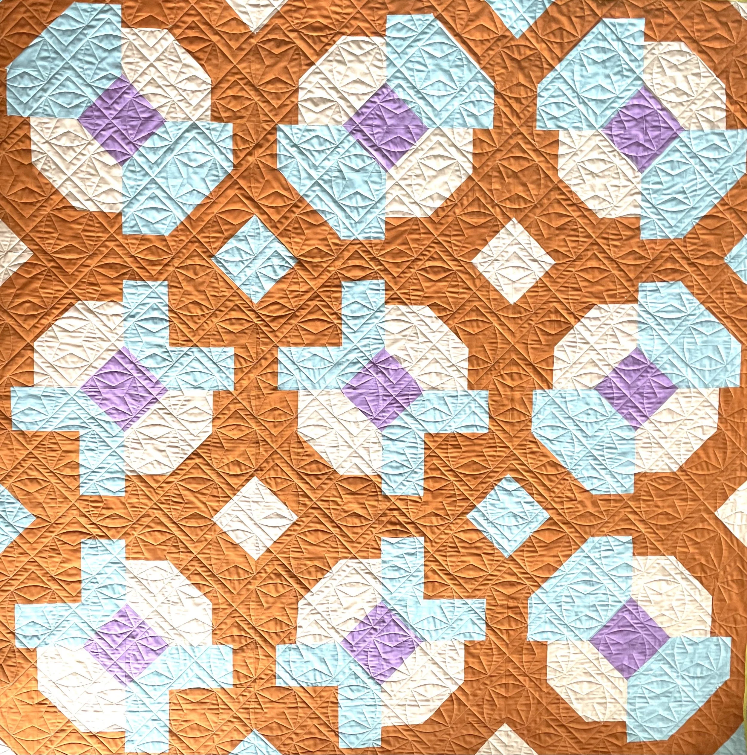 A colorful quilt with a geometric pattern featuring orange, white, purple, and blue shapes.