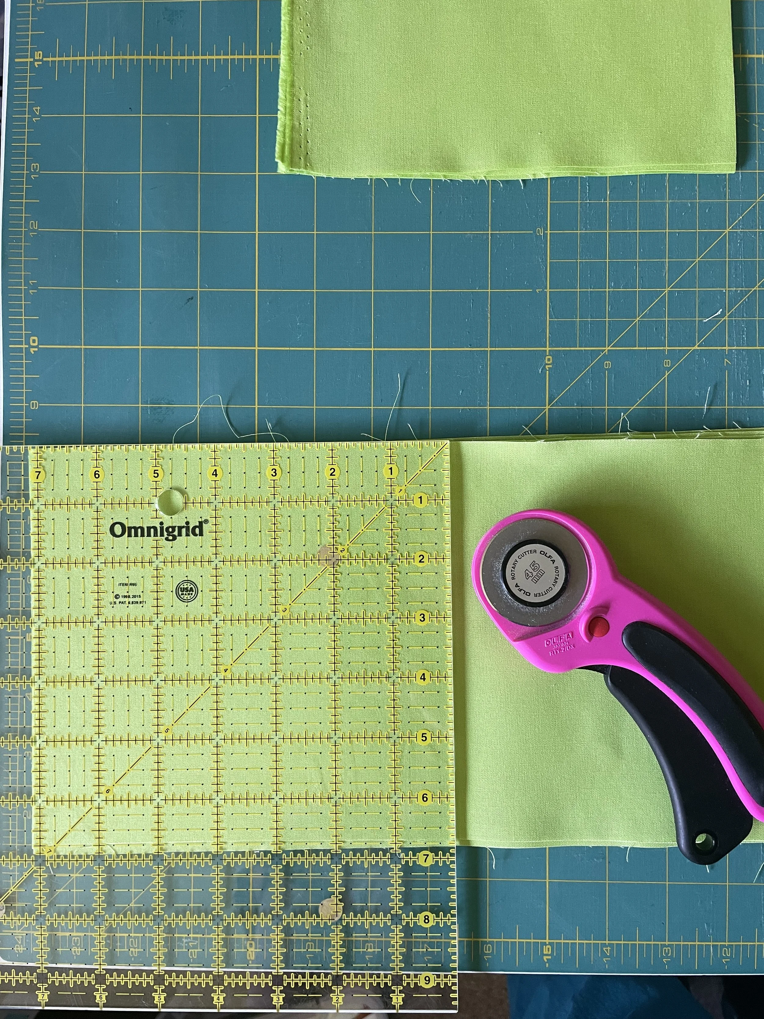 A quilting or sewing workspace with a yellow ruler, a cutting tool, and fabric pieces on a green cutting mat.