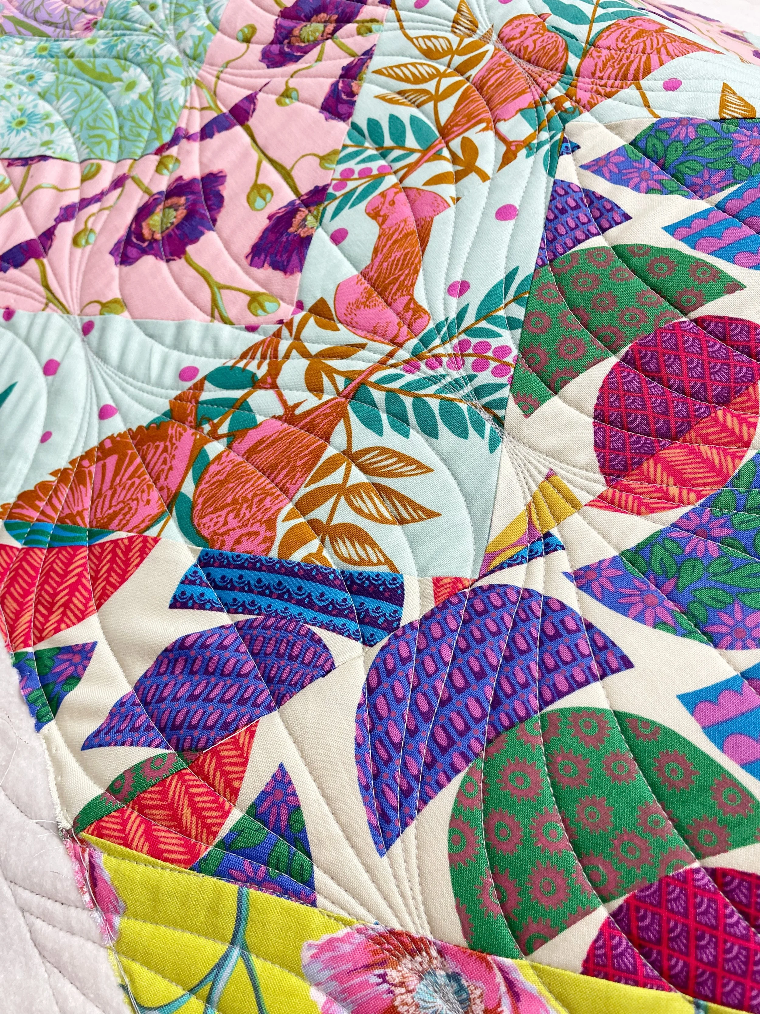Close-up of a colorful patchwork quilt with floral and geometric patterns in pink, purple, green, blue, orange, and yellow.
