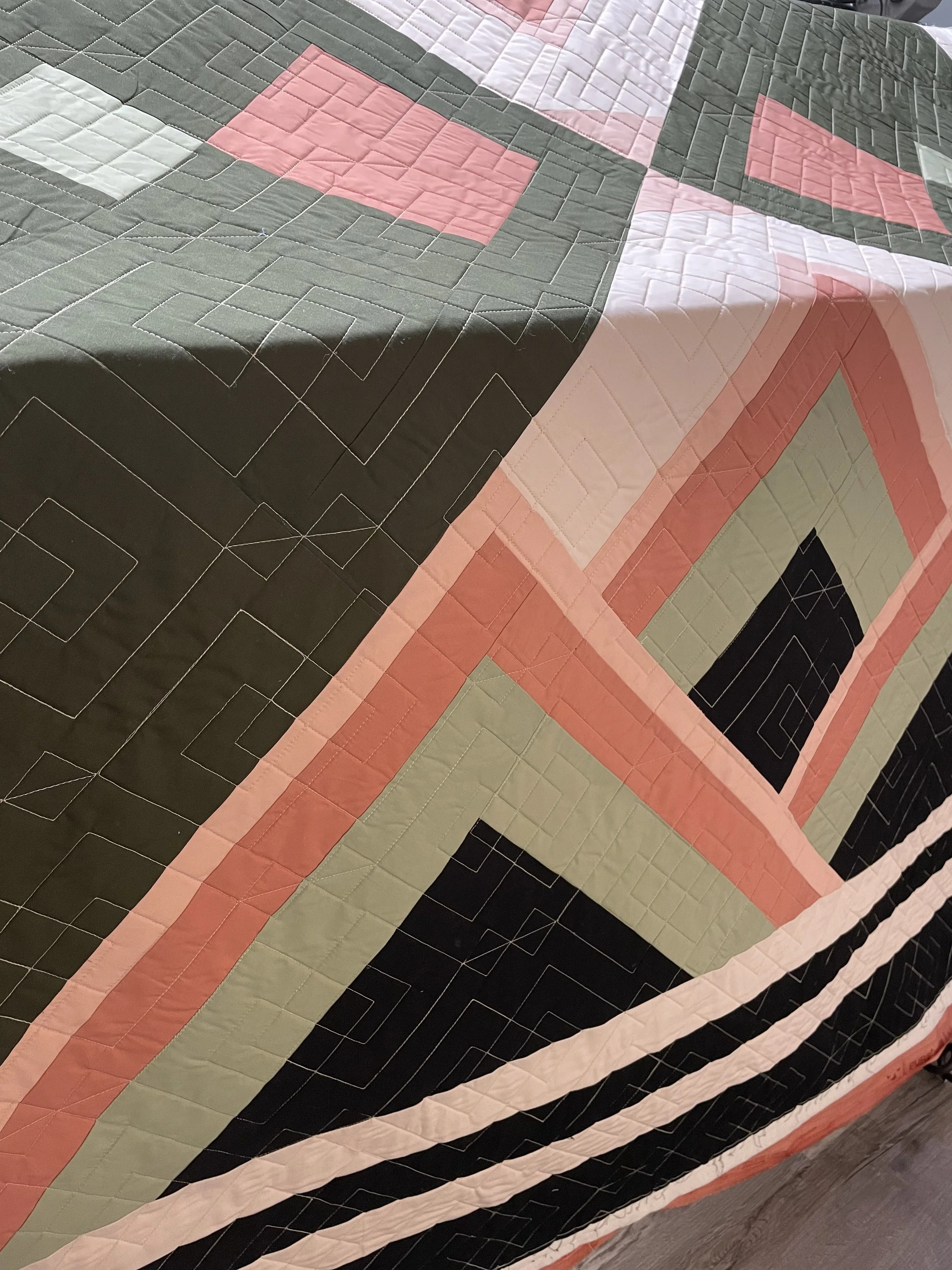Close-up of a quilt with geometric patterns in shades of pink, green, black, and white.
