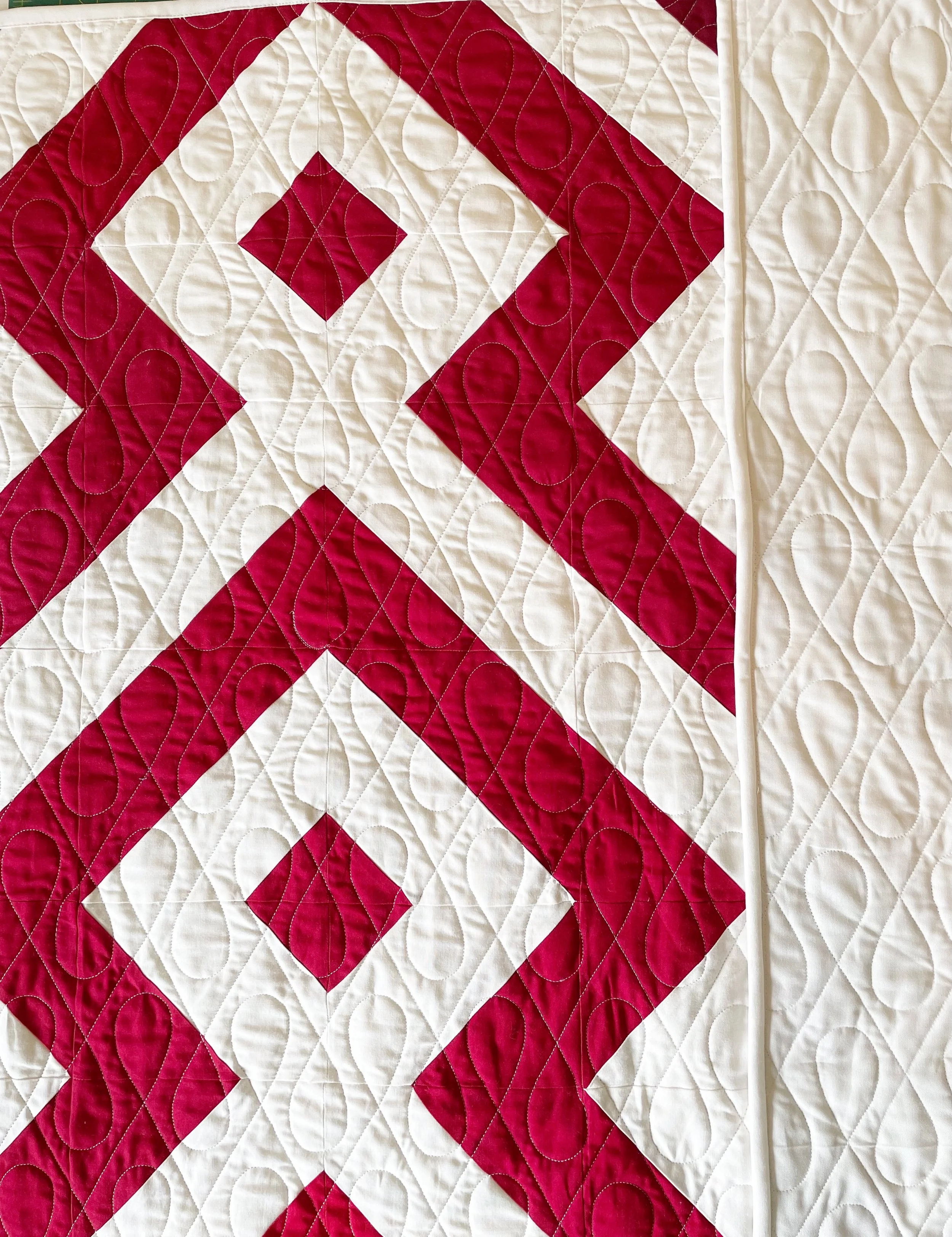 Close-up of a quilt with a red and white geometric pattern, featuring diamond shapes and intricate quilting stitches.