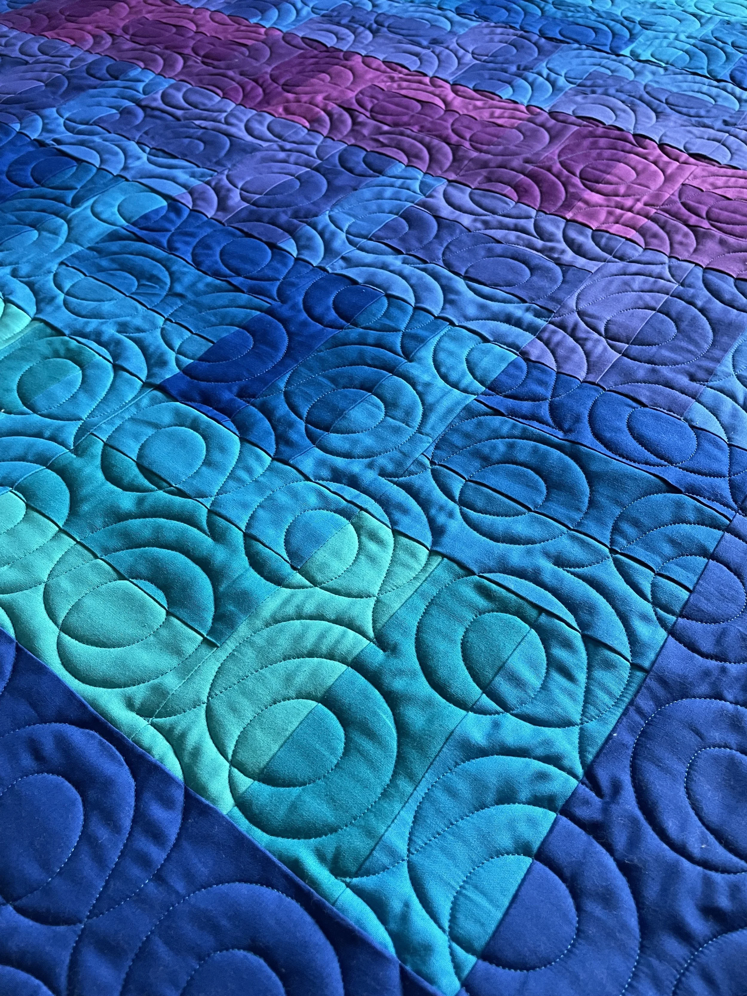 Close-up of a colorful quilt with a pattern of overlapping circles in shades of blue, purple, and teal.