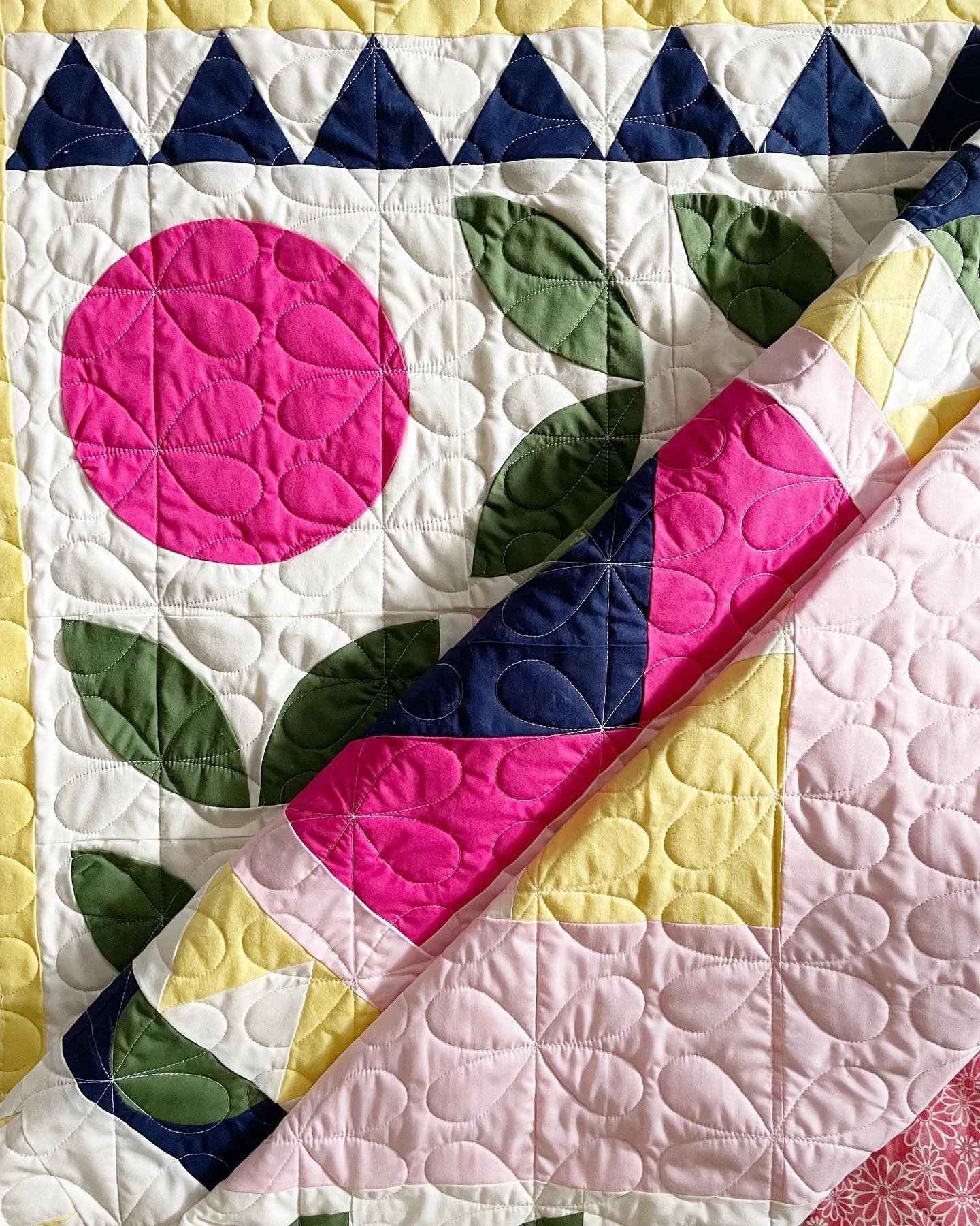 Colorful quilt featuring a pink flower with green leaves and a pieced pink, yellow, blue, and white design.