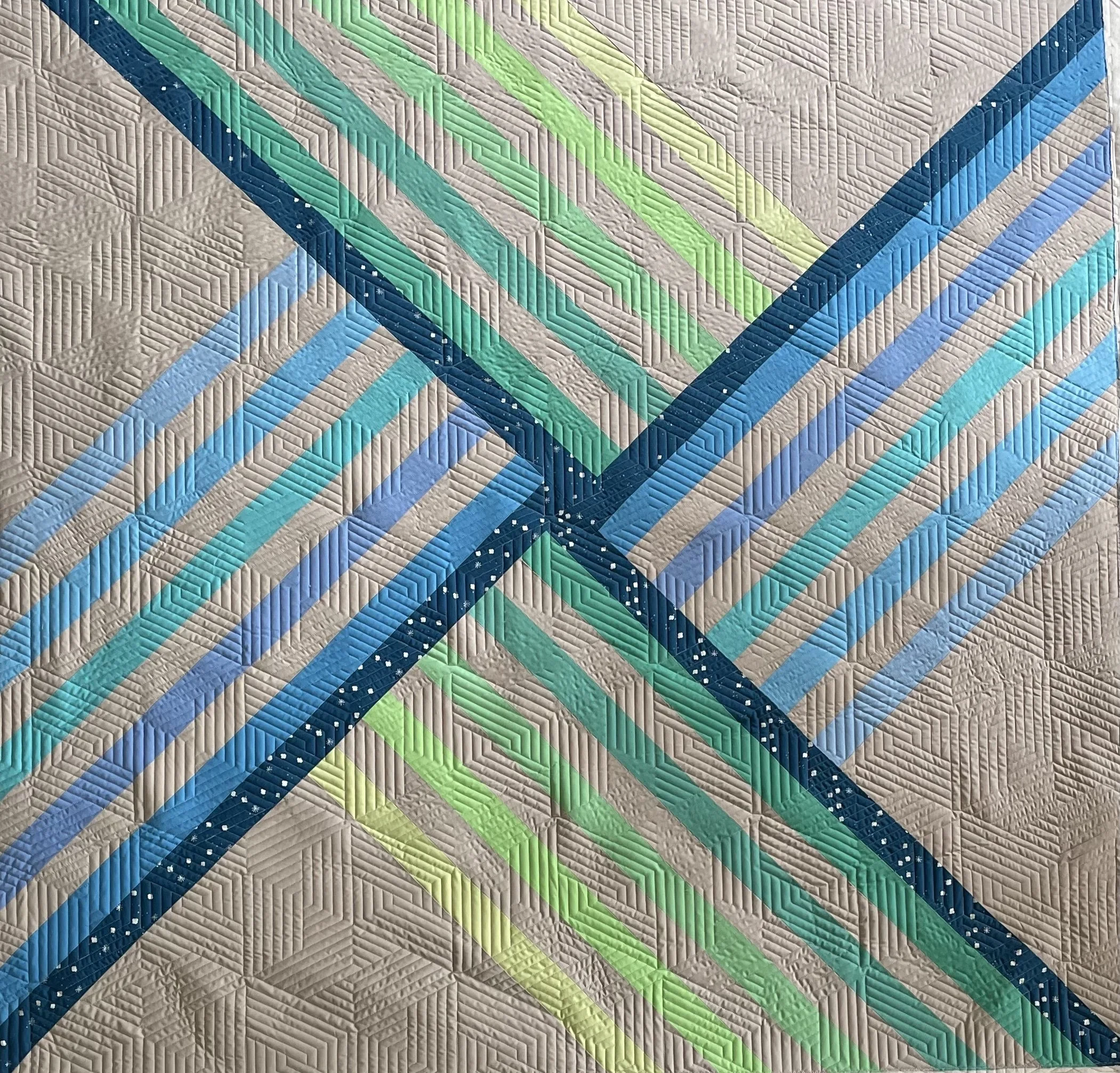 Close-up of a colorful geometric quilt with diagonal stripes in shades of green, blue, and beige, arranged in a symmetrical pattern.
