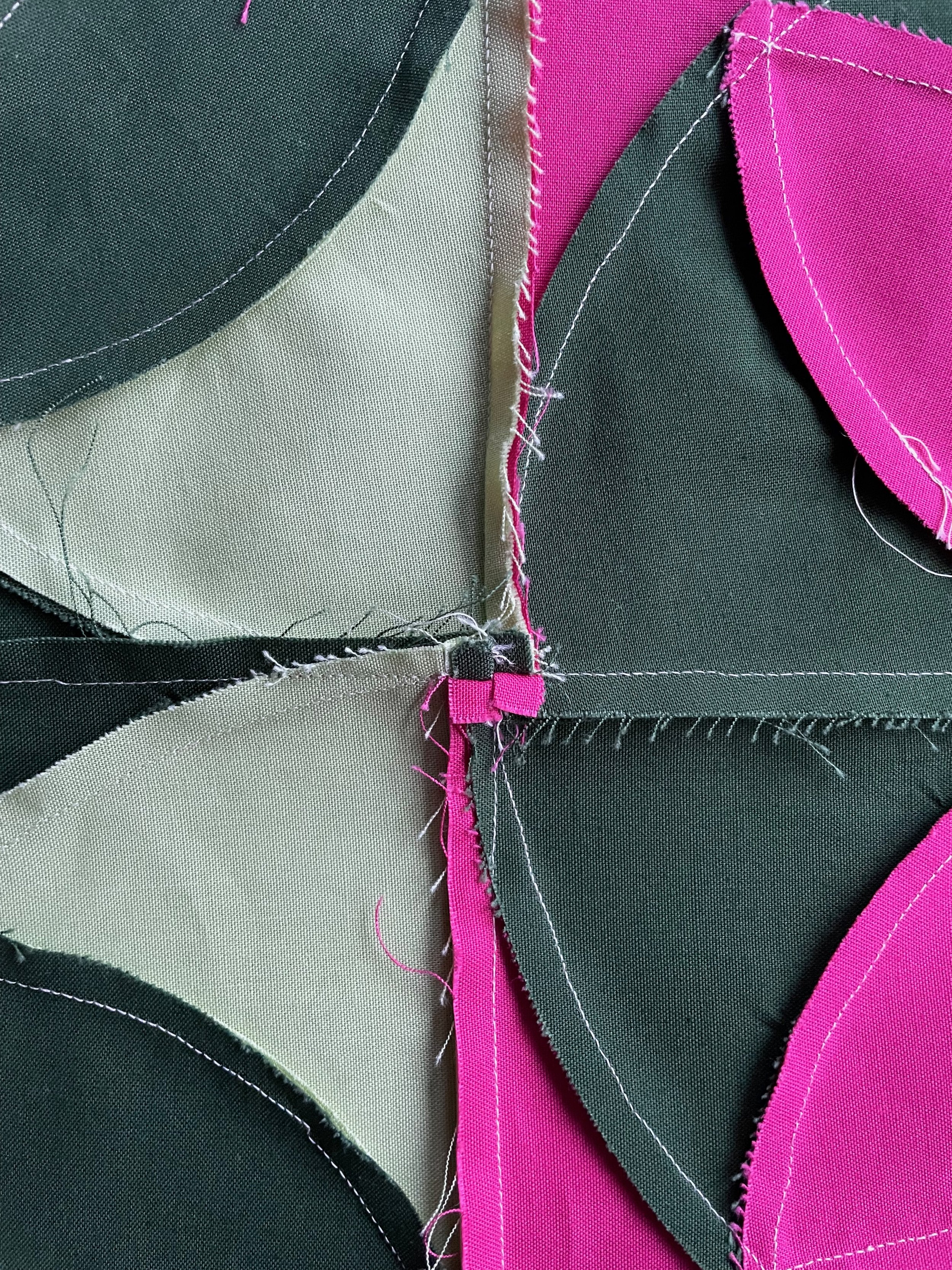 Close-up of fabric pieces sewn together with visible pink, black, and beige fabrics and white stitching.