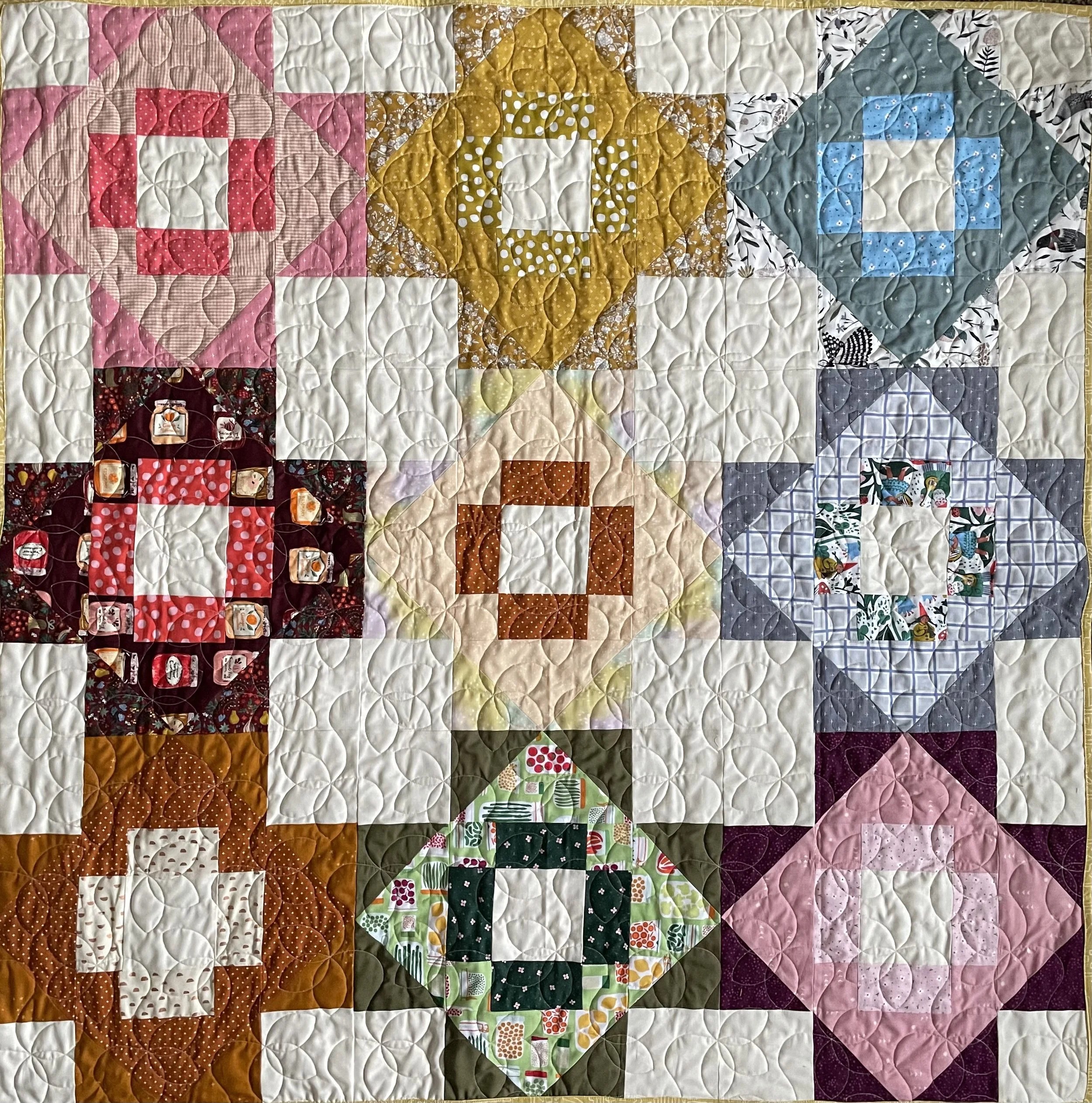 A colorful patchwork quilt with various patterns and shapes, including diamonds, squares, and crosses, in different colors such as pink, yellow, red, green, blue, purple, and white.