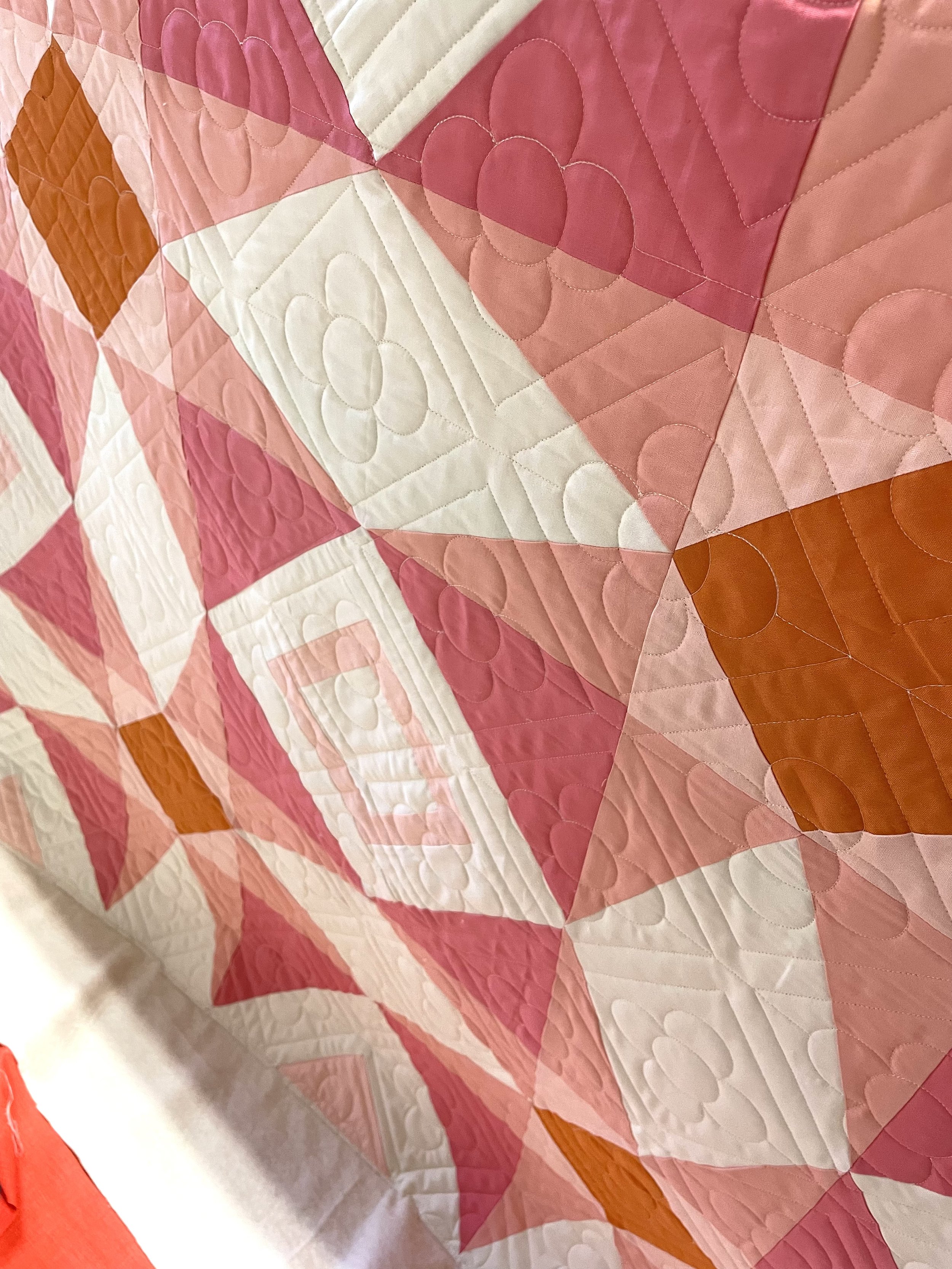 Close-up of a quilt with pink, white, and orange geometric and floral patterns.