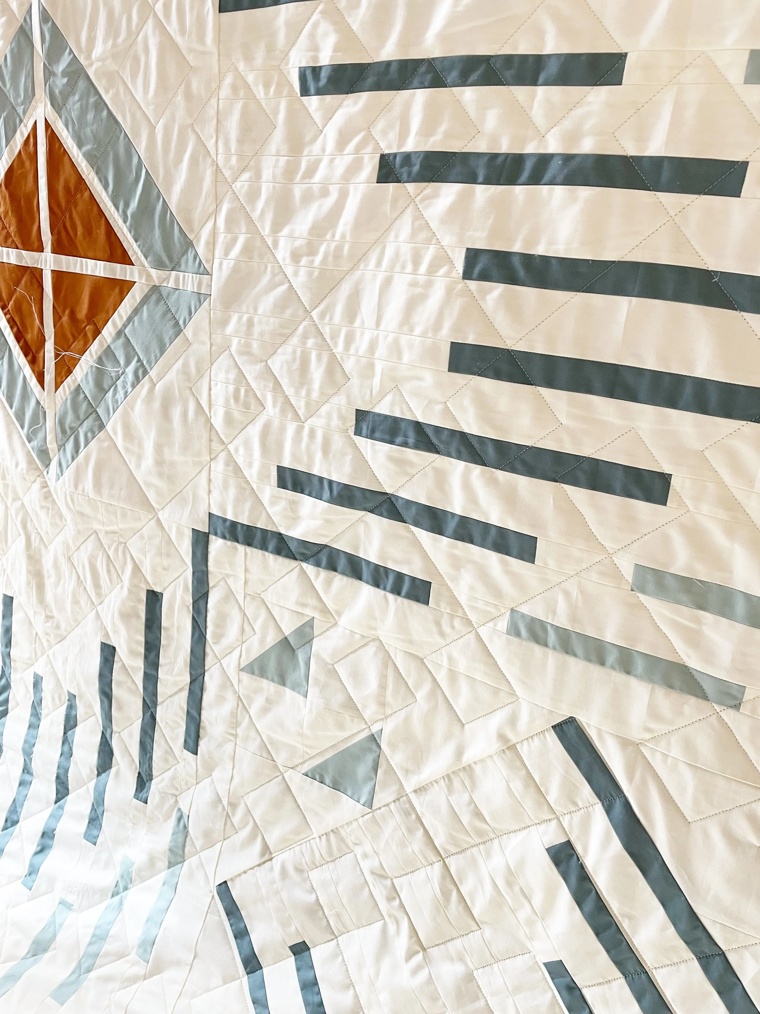 Close-up view of a quilt with geometric patterns, including diamonds and lines, in beige, gray, and brown colors.