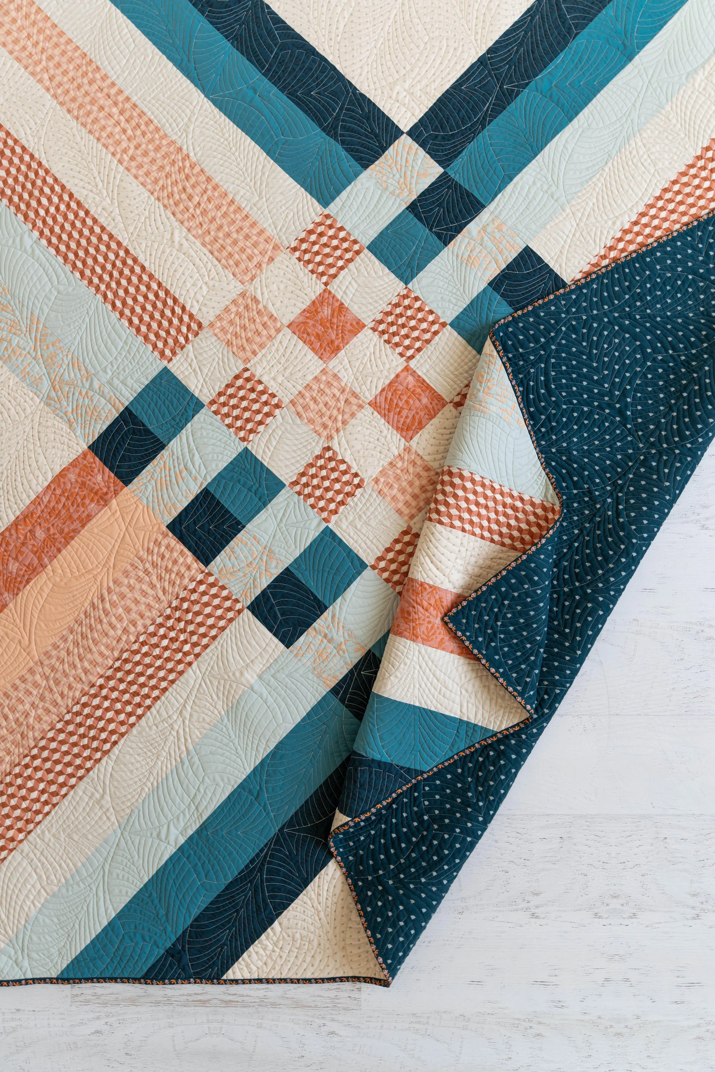 Close-up of a multicolored patchwork quilt with geometric patterns and quilting stitches, partially folded over a white wooden surface.