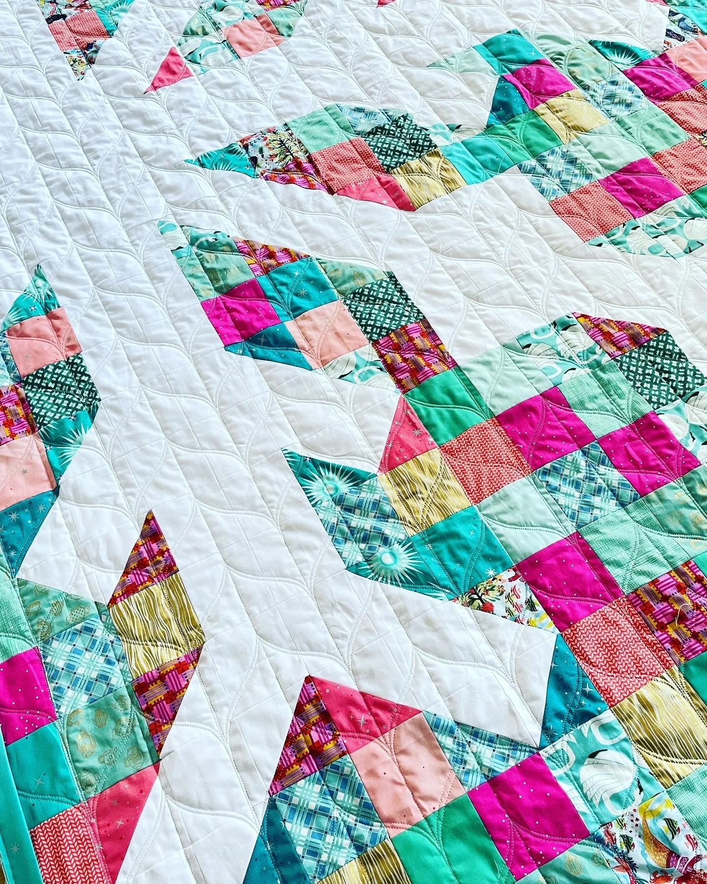 Close-up of a colorful quilt with patterns and shapes on a white background, featuring a mix of bright pinks, greens, blues, and other colors.