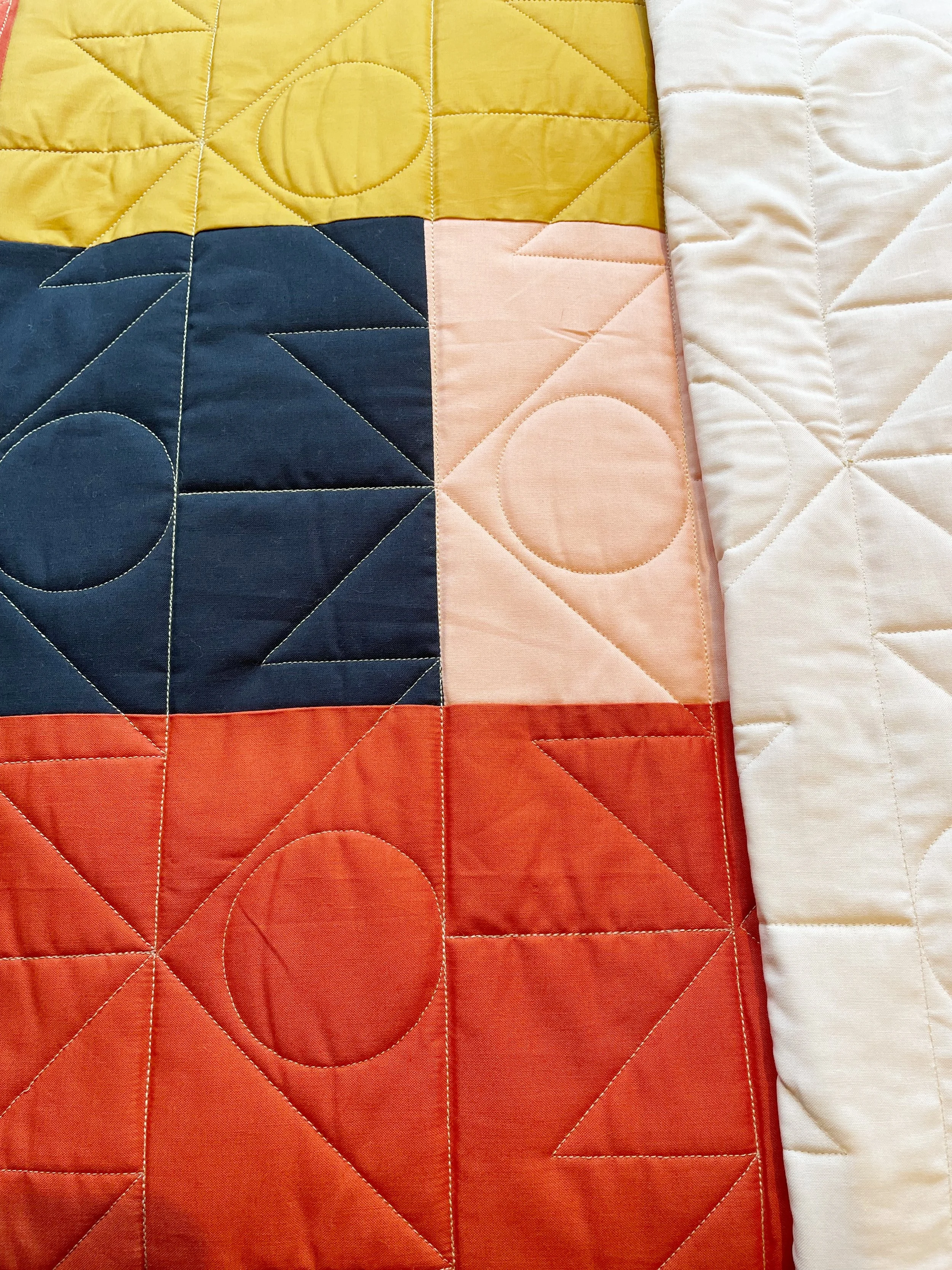 Close-up of a quilt with colorful geometric patterns including circles and triangles in yellow, blue, pink, red, and white sections.