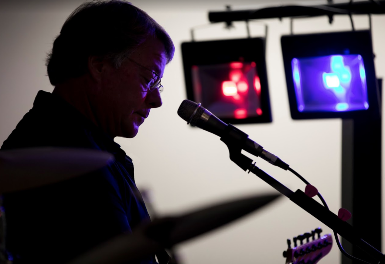Silhouette of a man speaking into a microphone with colorful lights in the background.