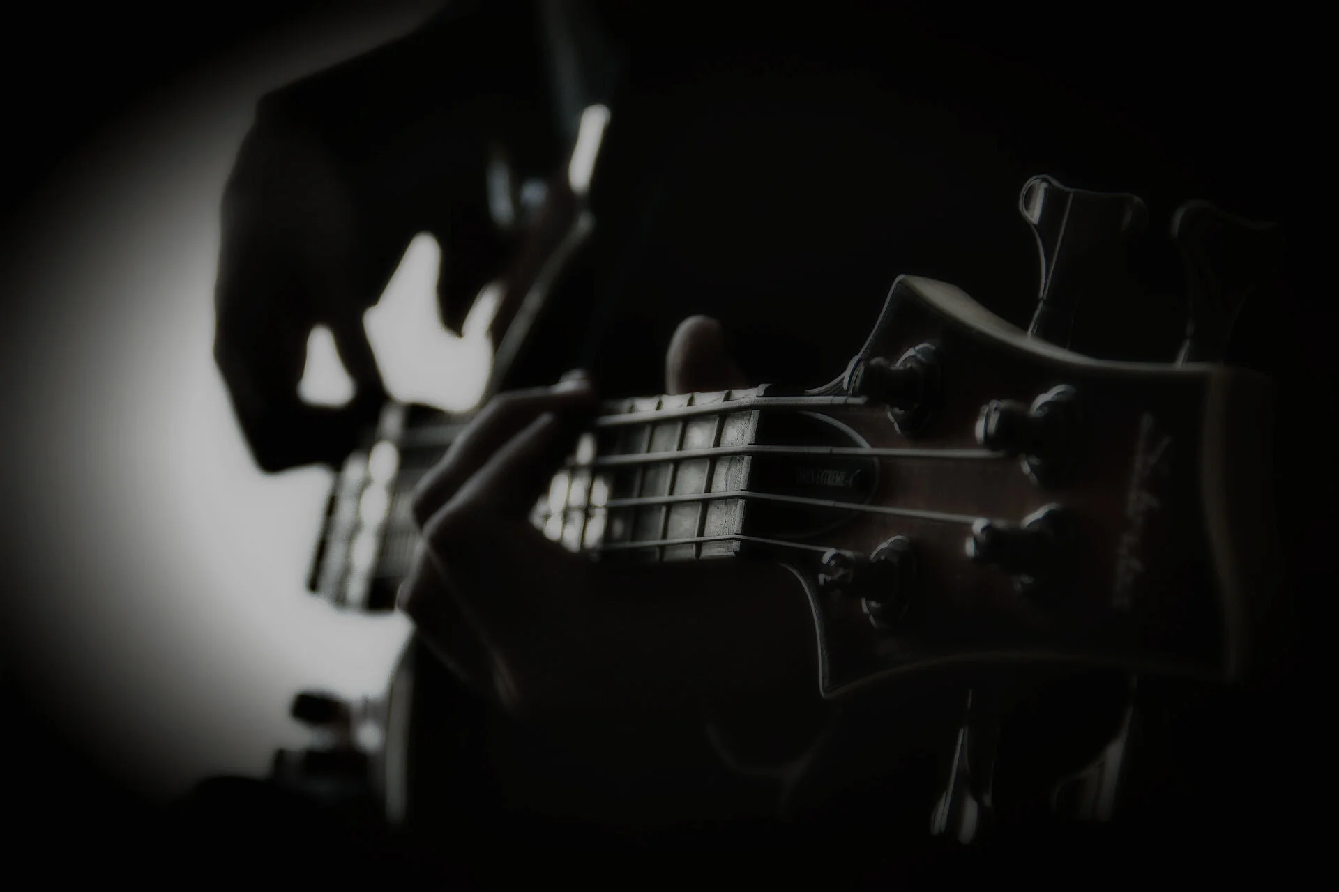 Close-up of a person playing a guitar in a dark setting, with focus on the headstock and hand on the fretboard.