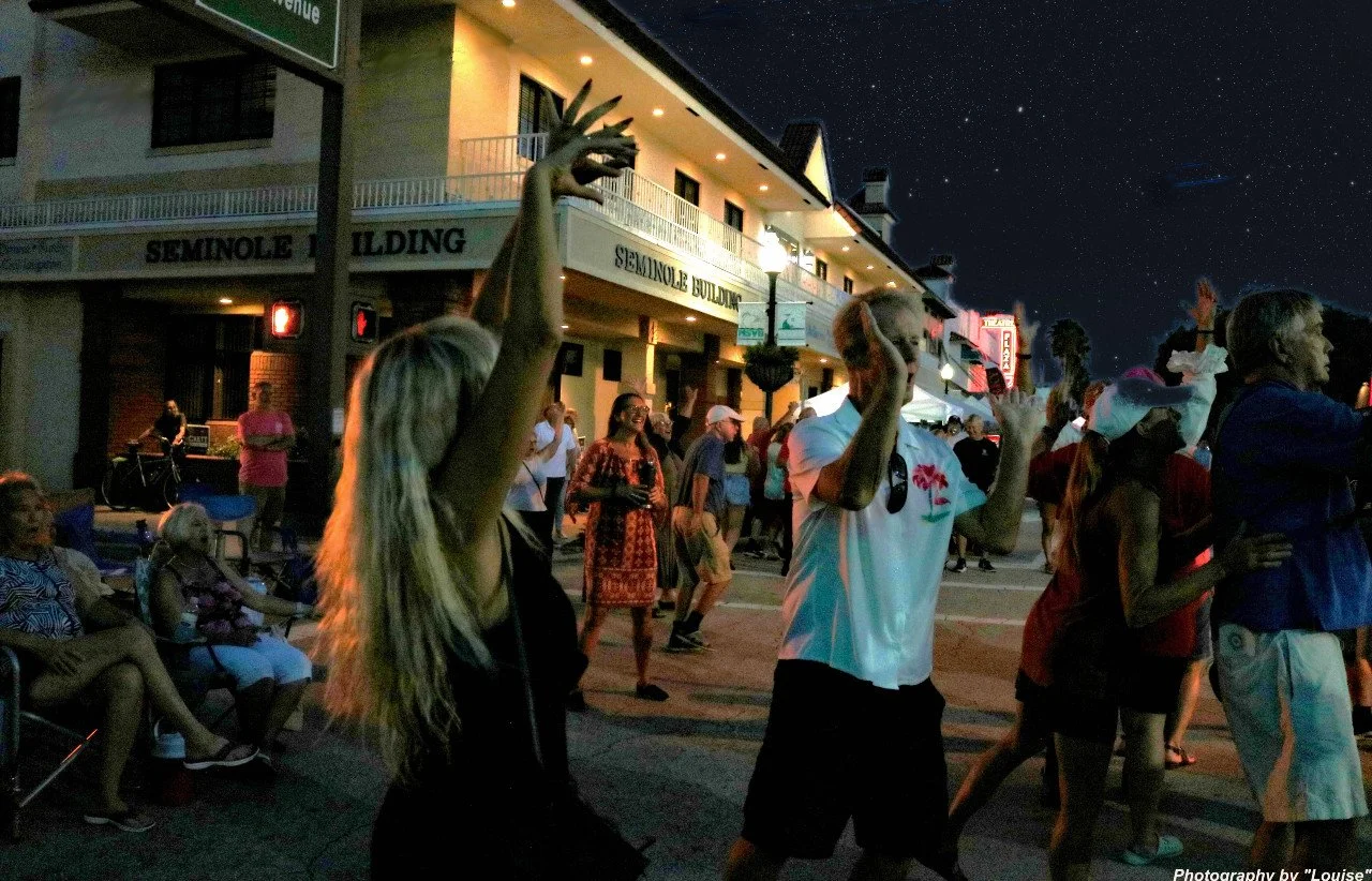 People dancing and enjoying a street event at night with a Seminole Building in the background and stars visible in the sky.