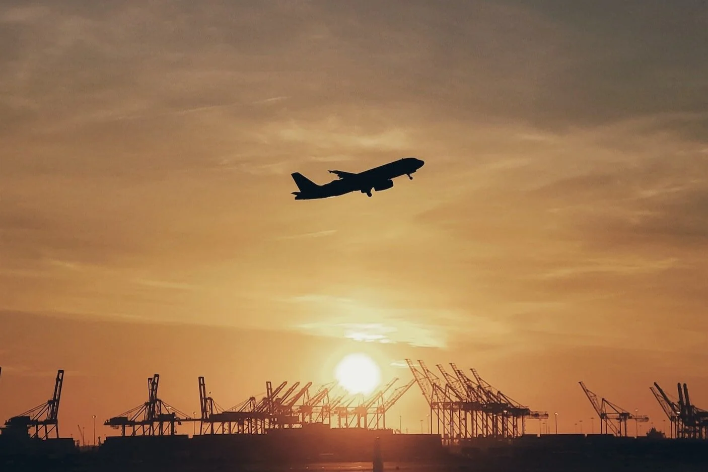 An airplane taking off above a port at sunset.